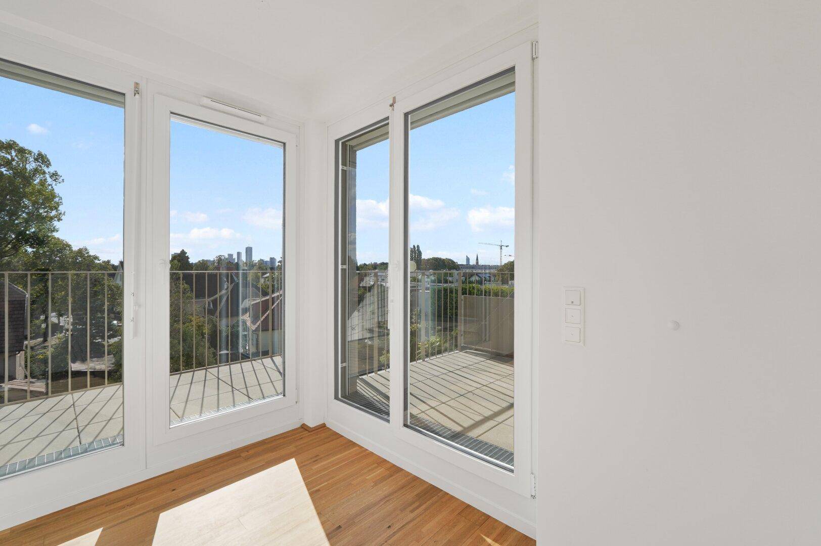 Heller Raum mit Holzboden und raumhohen Fenstern, die Zugang zu einem Balkon bieten.