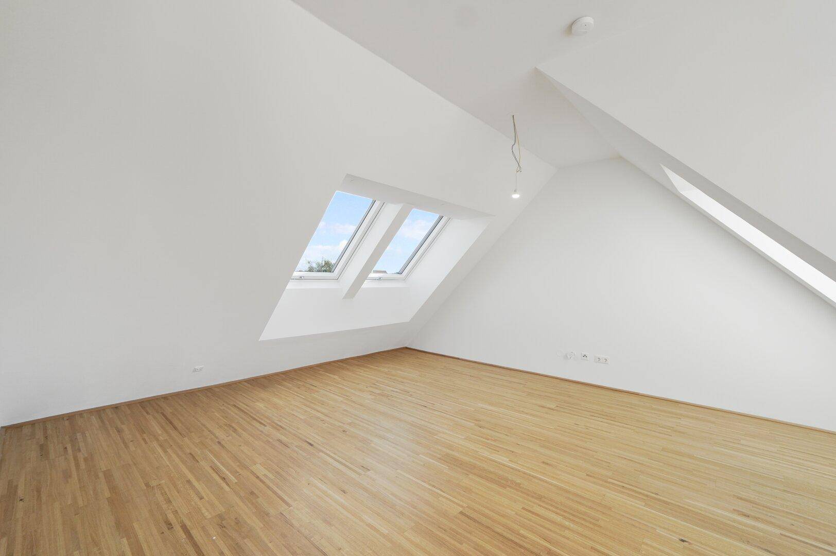 Geräumiger Raum mit Holzboden, Dachschrägen und zwei Dachfenstern für viel Tageslicht.
