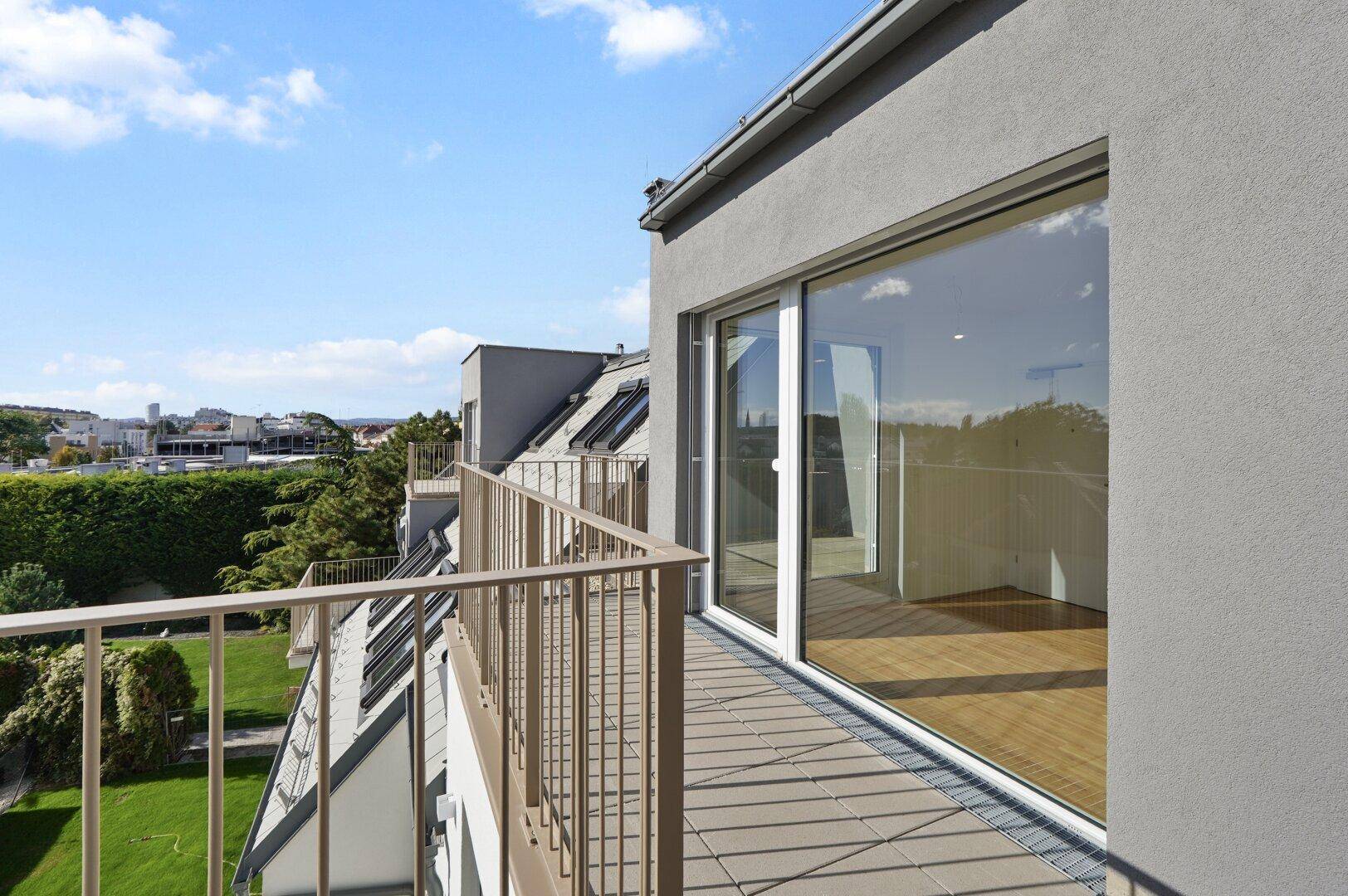 Geräumiger Balkon mit Fliesenboden und Blick auf grüne Umgebung und die Stadt.