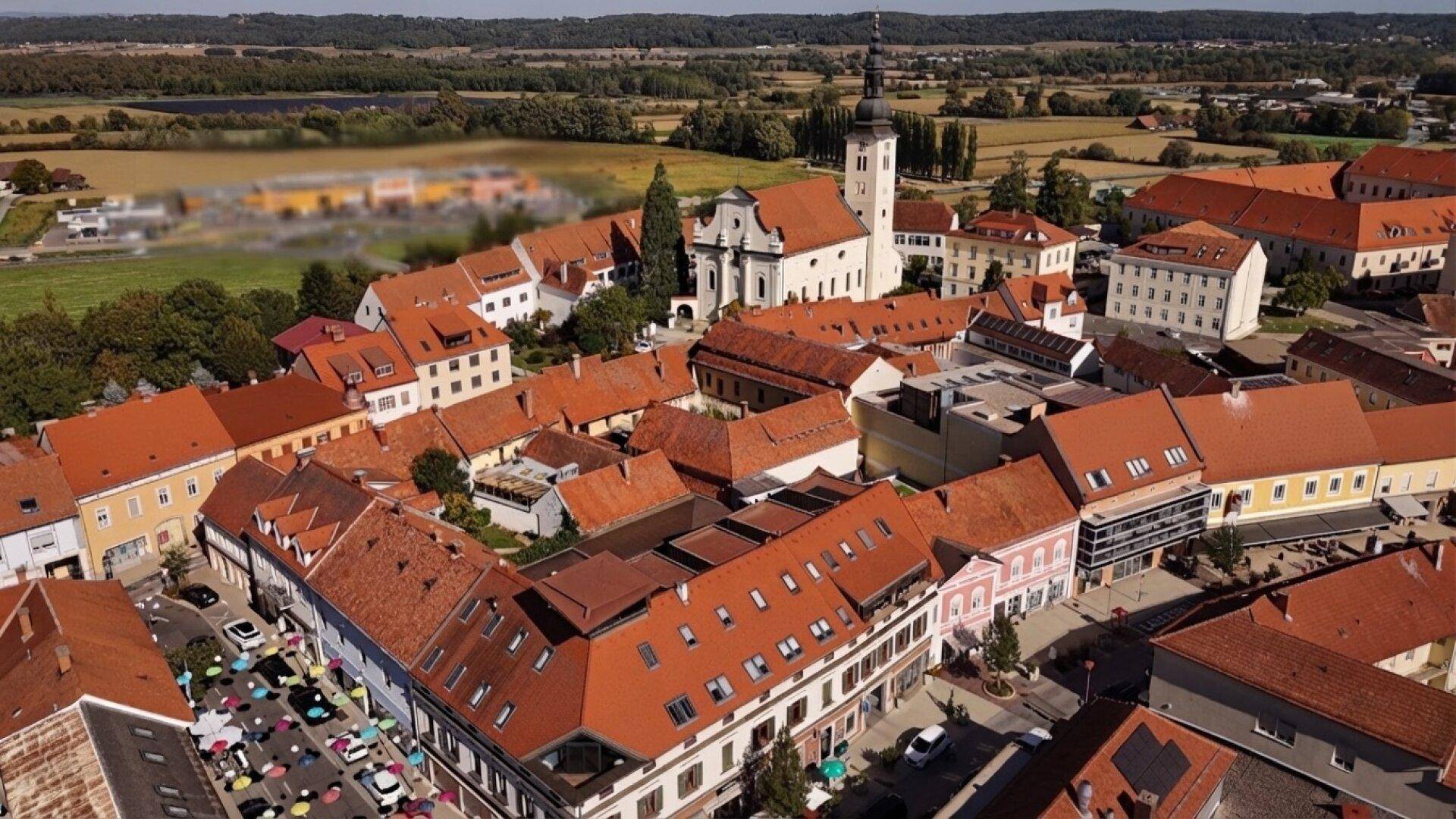 Luftaufnahme einer charmanten Stadt mit roten Dächern, einer historischen Kirche und grüner Landschaft im Hintergrund.