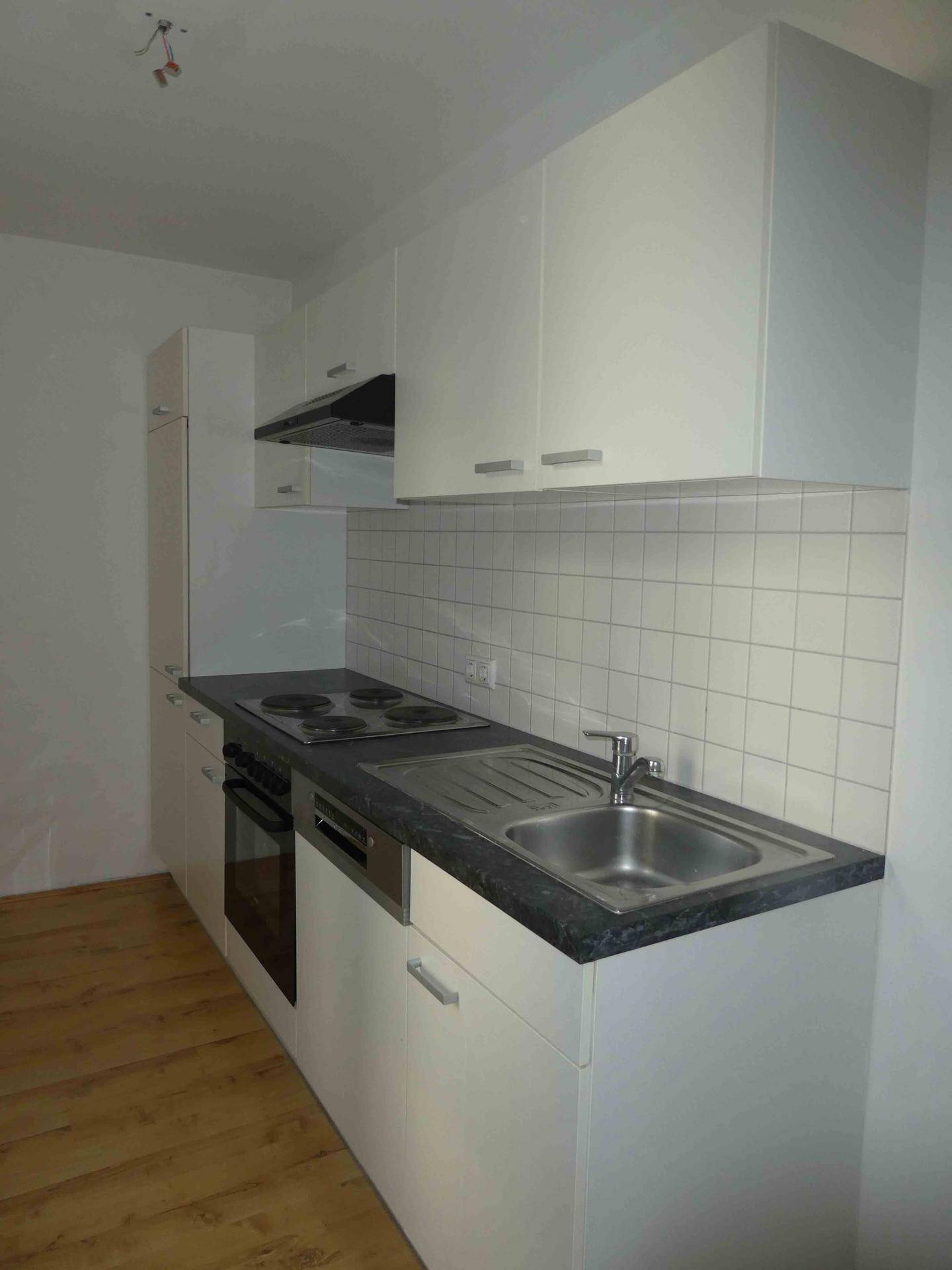 Moderne Einbauküche mit weißen Schränken, dunkler Arbeitsplatte und integrierten Geräten.