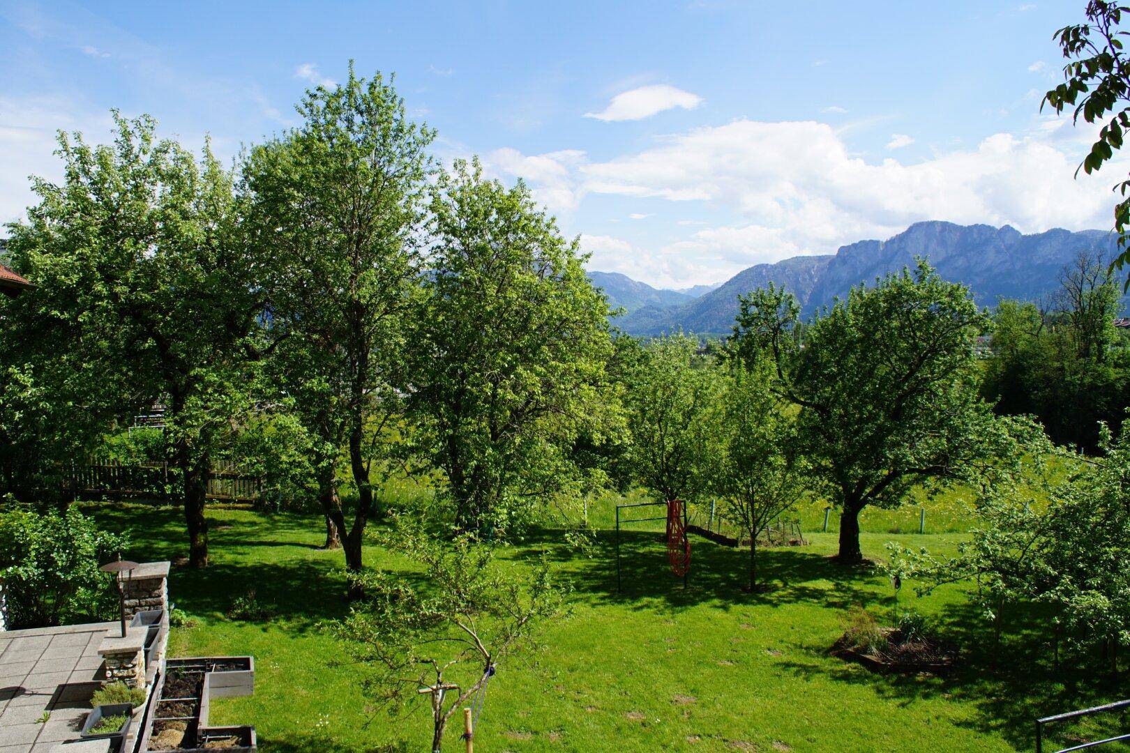Panoramablick vom Balkon auf den weitläufigen grünen Garten und die majestätischen Berge in der Ferne.