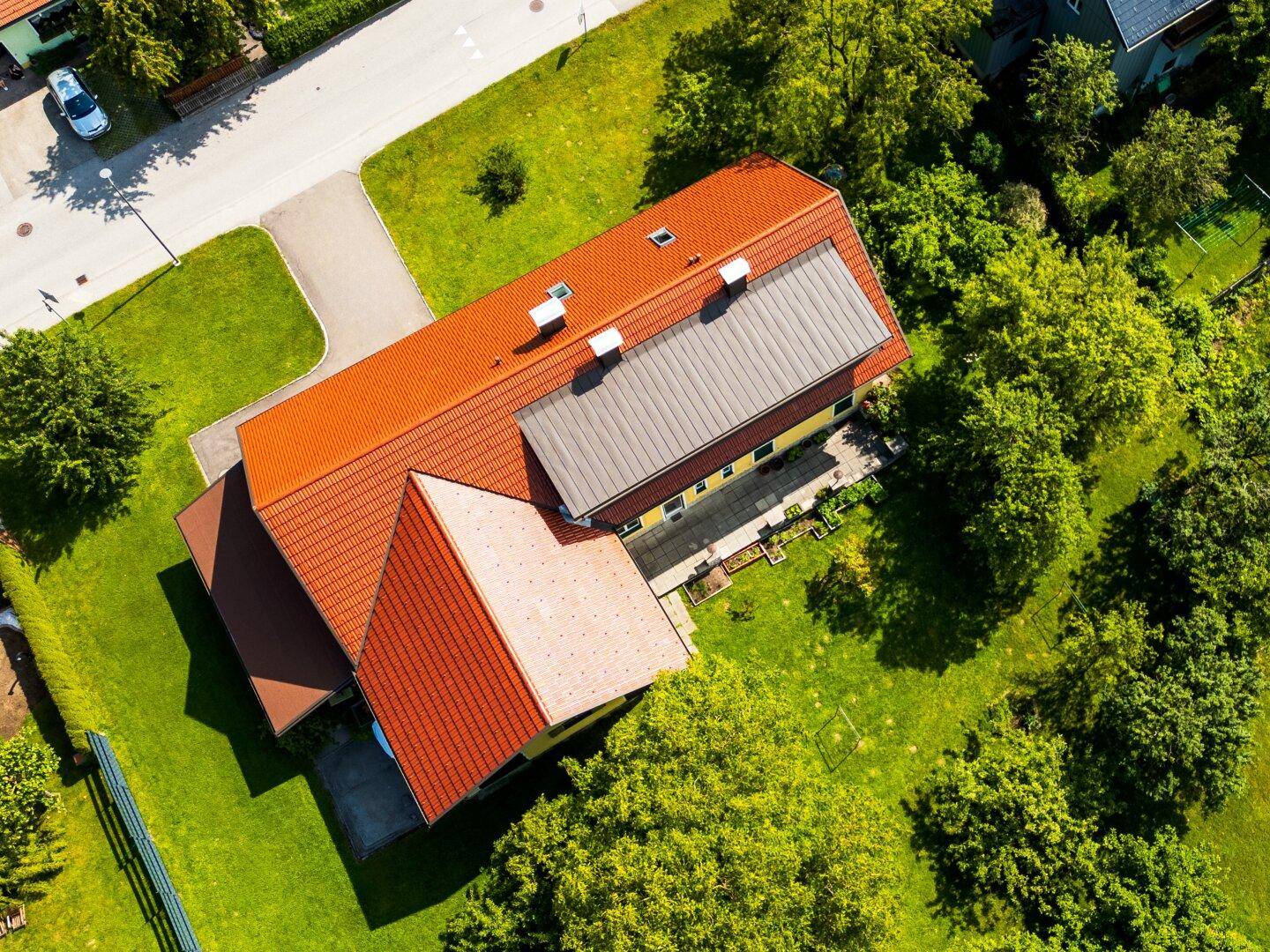 Luftaufnahme eines Hauses mit rotem Ziegeldach und großem grünen Gartenbereich.