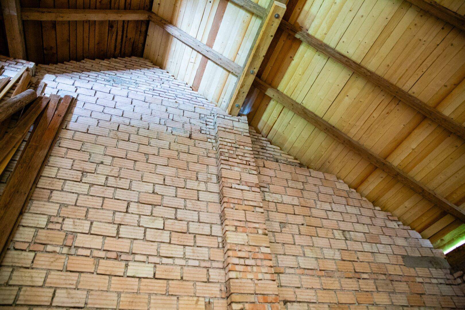Dachboden im Rohbau mit sichtbaren Ziegelwänden und freiliegenden Holzbalken der Dachkonstruktion.