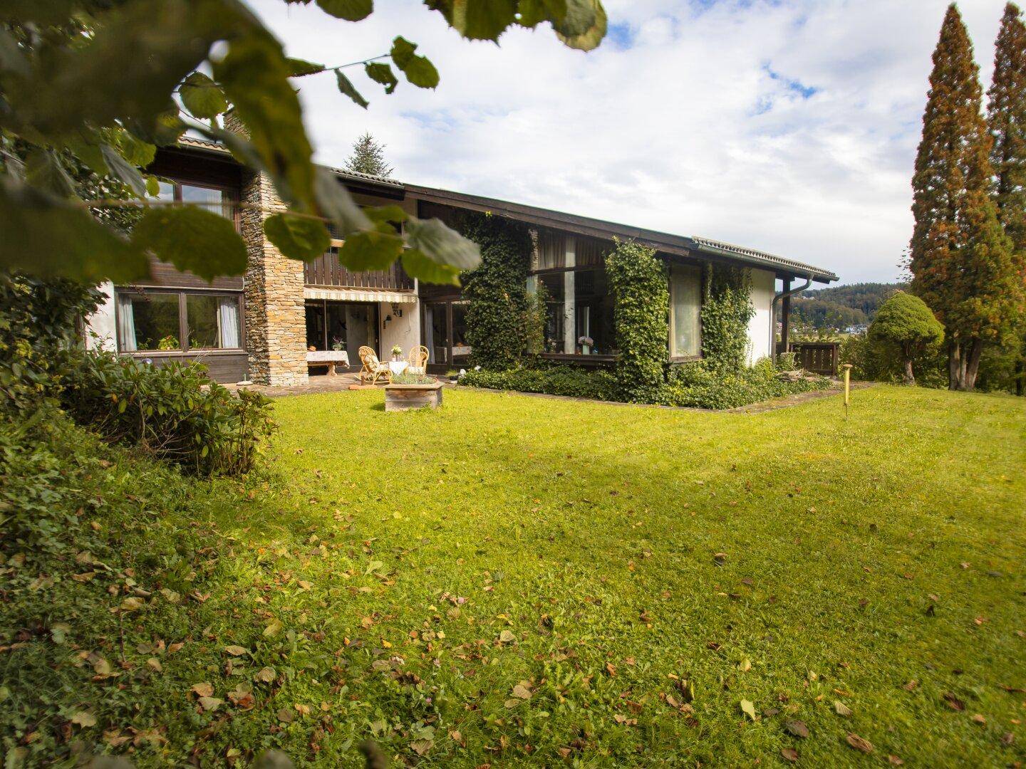 Großer grüner Gartenbereich neben dem Haus mit Rasenfläche und einer kleinen Sitzecke im Freien.