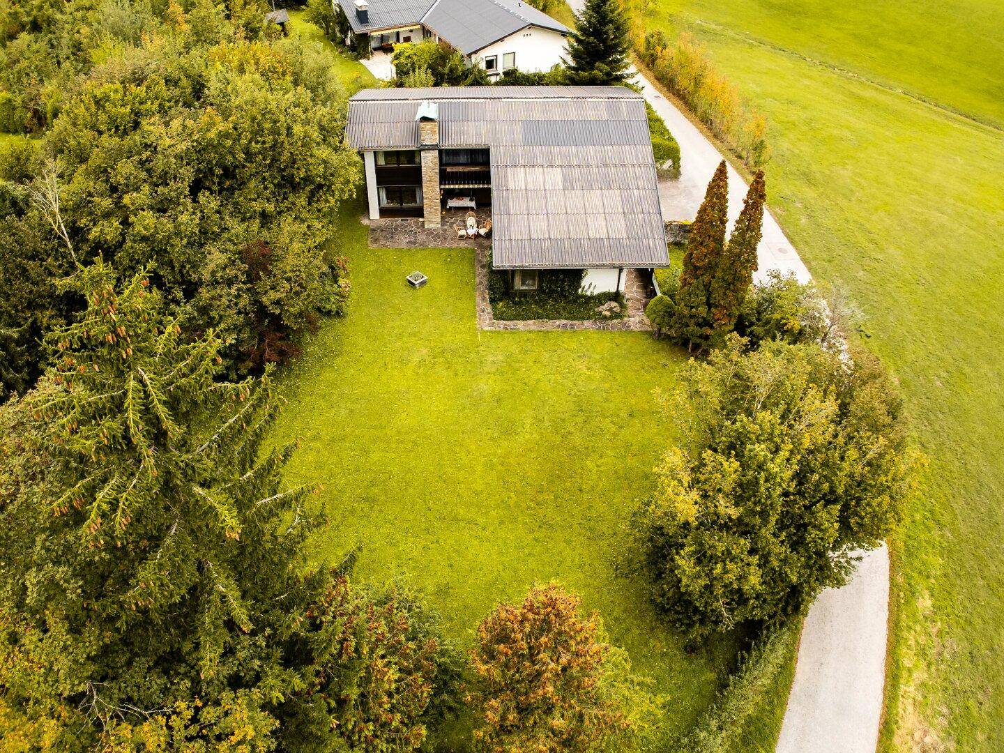 Luftaufnahme des Hauses mit großem Garten und umliegender grüner Landschaft unter blauem Himmel.