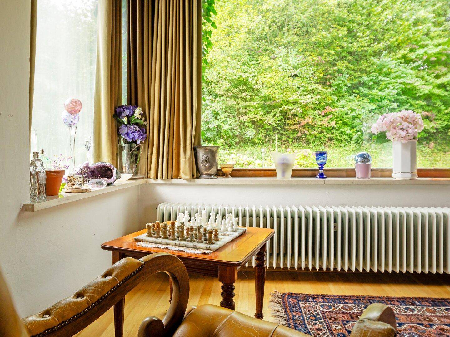 Fensterbereich im Wohnzimmer mit Schachspiel auf einem Tisch und einem Heizkörper unter dem Fenster.