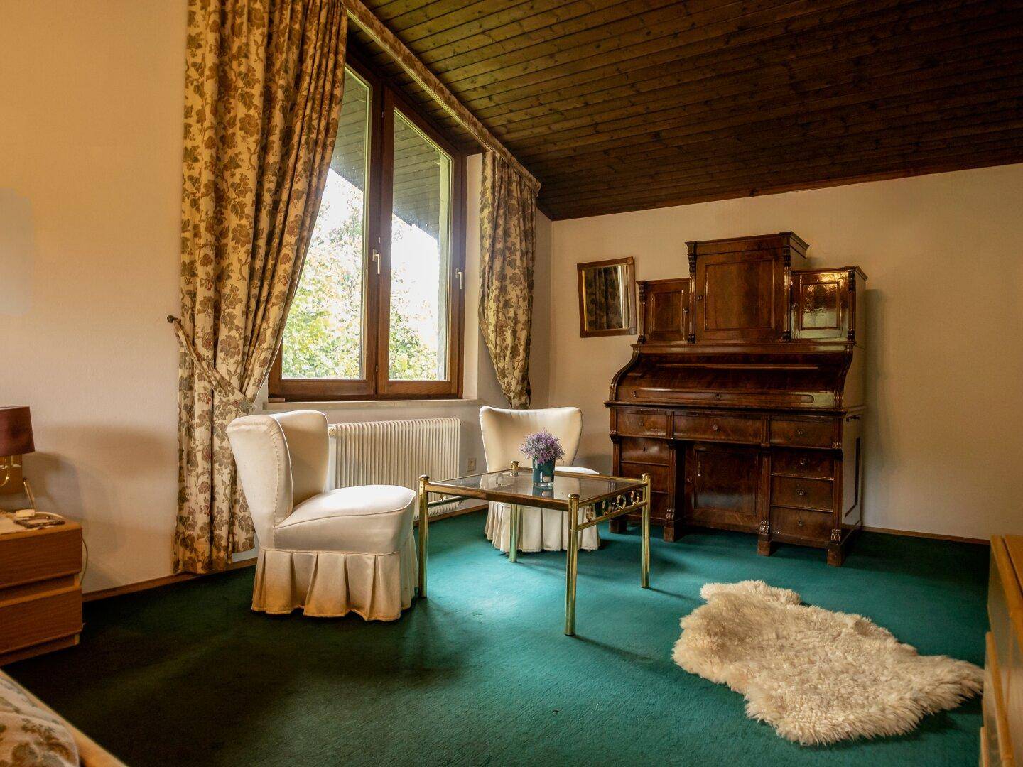 Schlafzimmer mit zwei Sesseln, einem kleinen Tisch und einem antiken Holzschreibtisch.