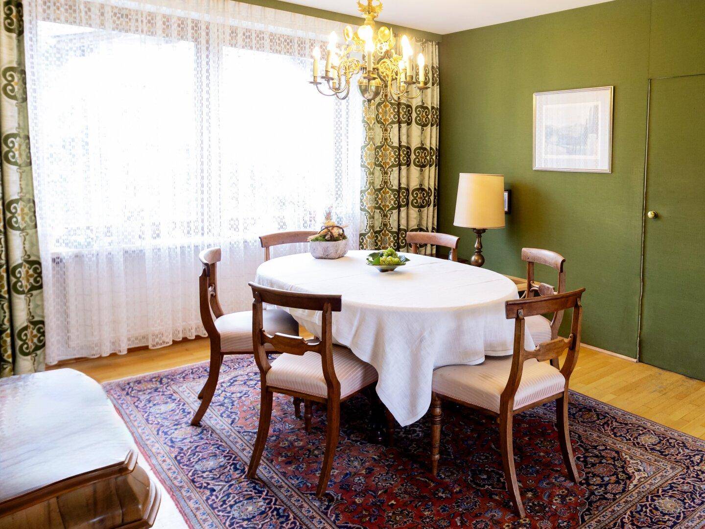 Esszimmer mit rundem Esstisch, grünen Wänden und gemusterten Vorhängen.