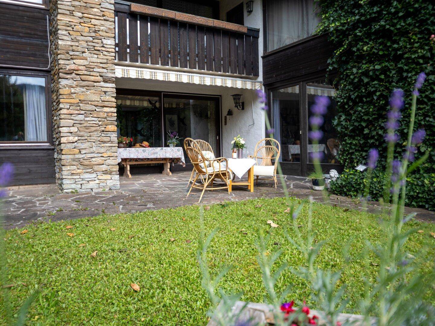 Gemütliche Terrasse mit Steinboden, Rattanmöbeln und angrenzendem Rasenbereich.