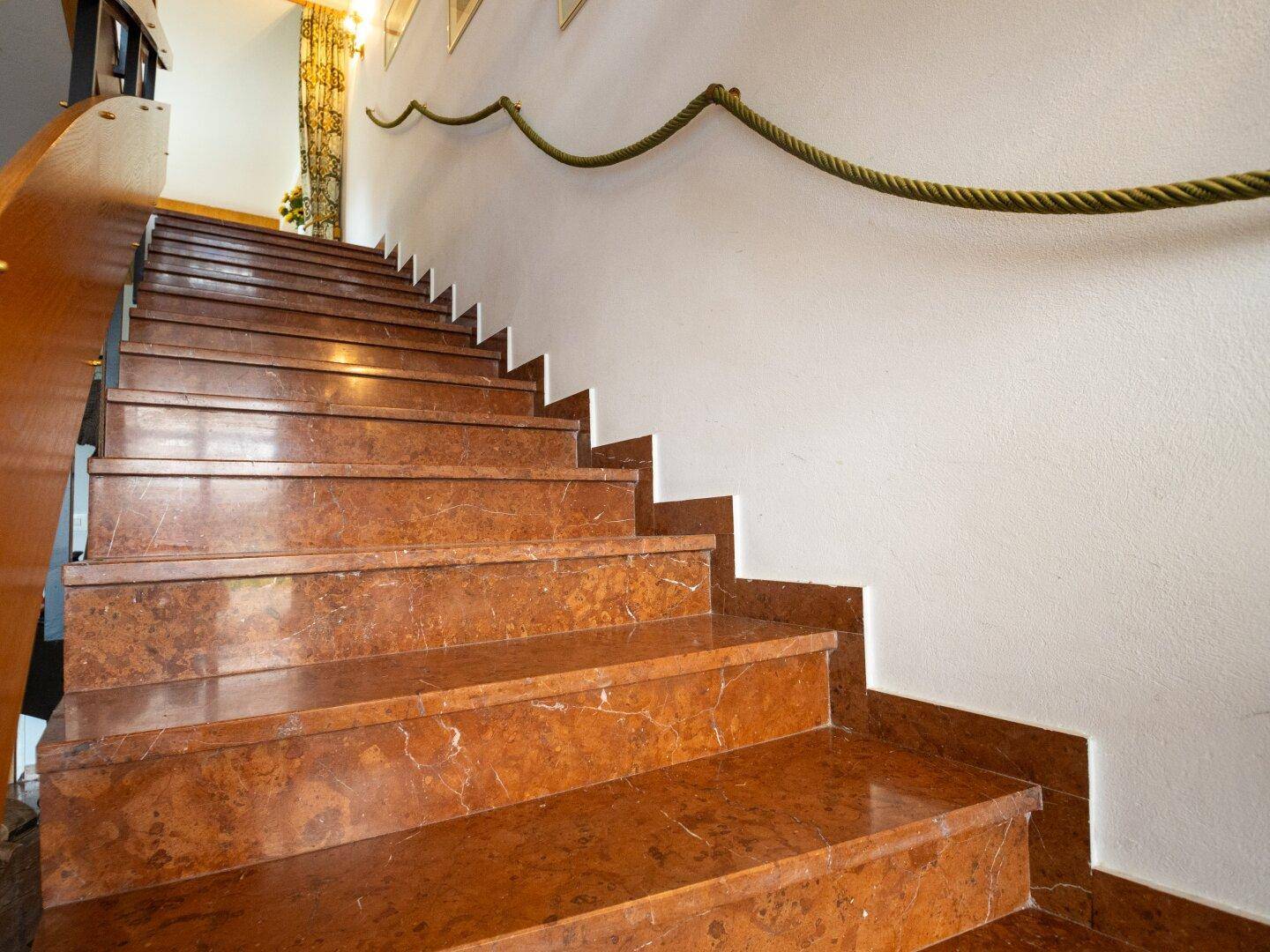 Elegante Treppe mit braunen Marmorstufen und einem Seilgeländer an der Wand.