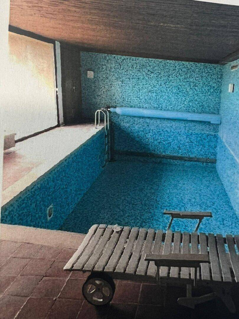 Innenpool mit blauen Fliesen, Holzdecke und einer Liege am Beckenrand.