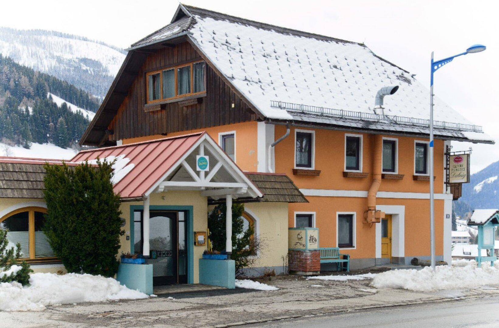 Traditionelles Gebäude mit orangefarbener Fassade und schneebedecktem Dach in einer winterlichen Berglandschaft.