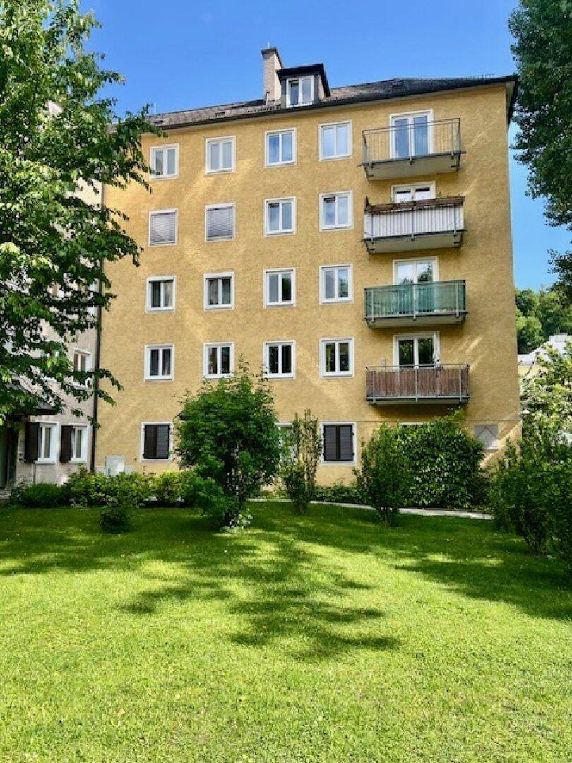 Gelbes Mehrfamilienhaus mit mehreren Balkonen und einer gepflegten Rasenfläche im Vorgarten.