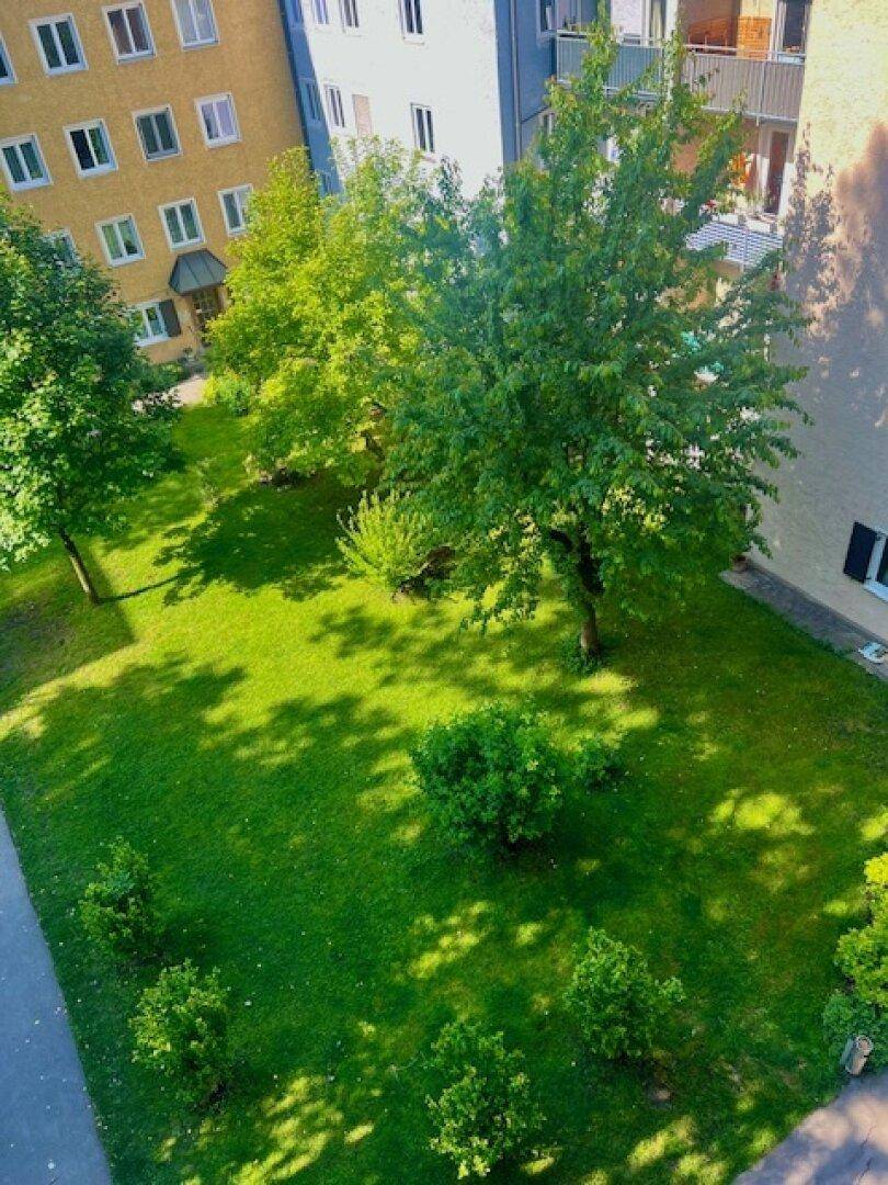 Blick von oben auf einen grünen Innenhof mit Bäumen und Rasenflächen, umgeben von Wohngebäuden.