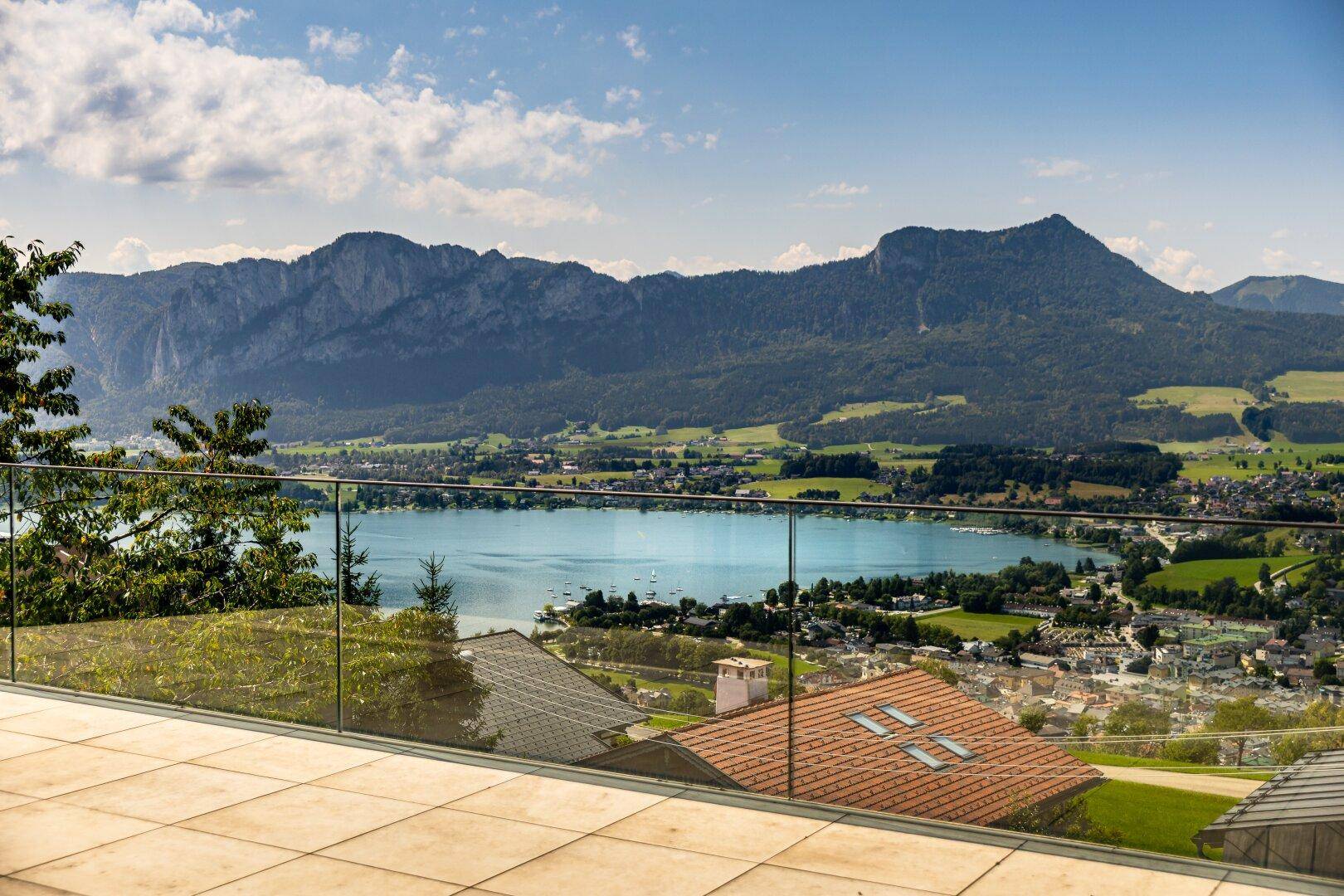 Geräumige Terrasse mit Fliesenboden und Glasbrüstung bietet einen weiten Blick auf den Mondsee und die umliegende Bergwelt.