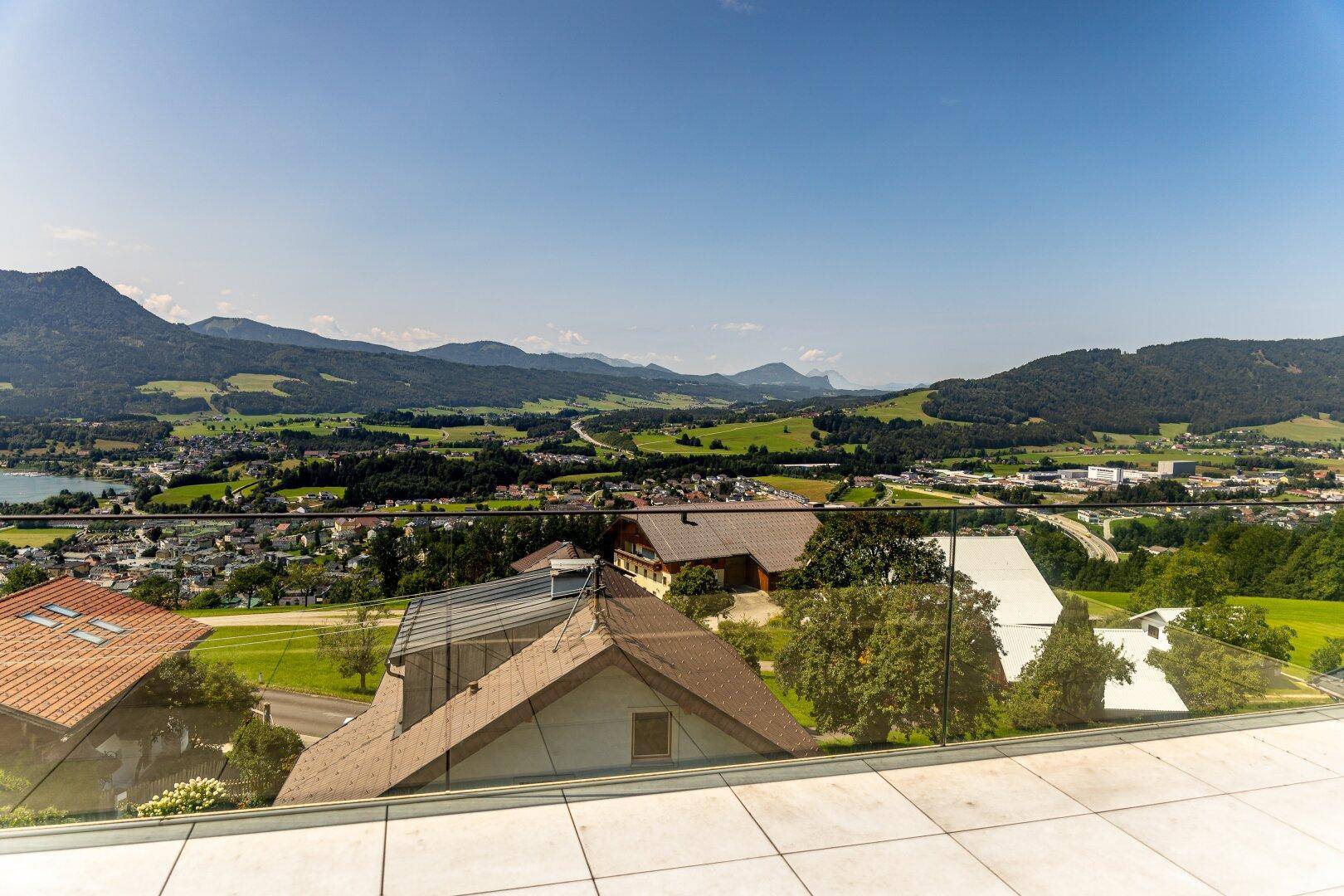 Weitläufige Terrasse mit Fliesenboden und Glasgeländer bietet einen atemberaubenden Blick auf den See und die Berge.