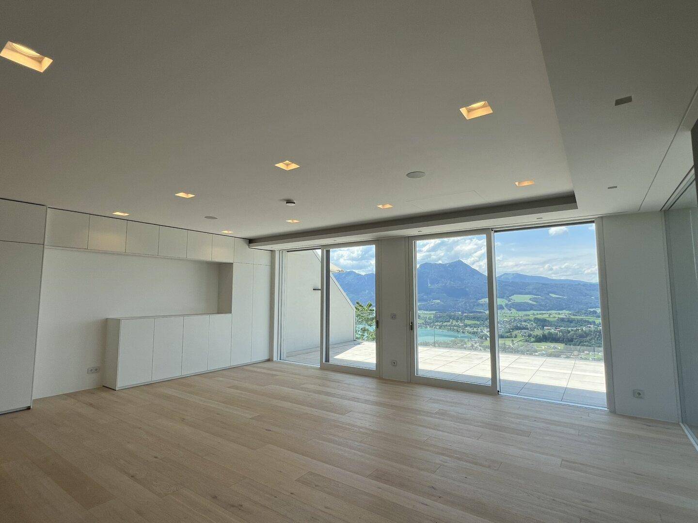 Lichtdurchfluteter Wohnraum mit Einbauschränken und weitem Blick auf Berge und See.