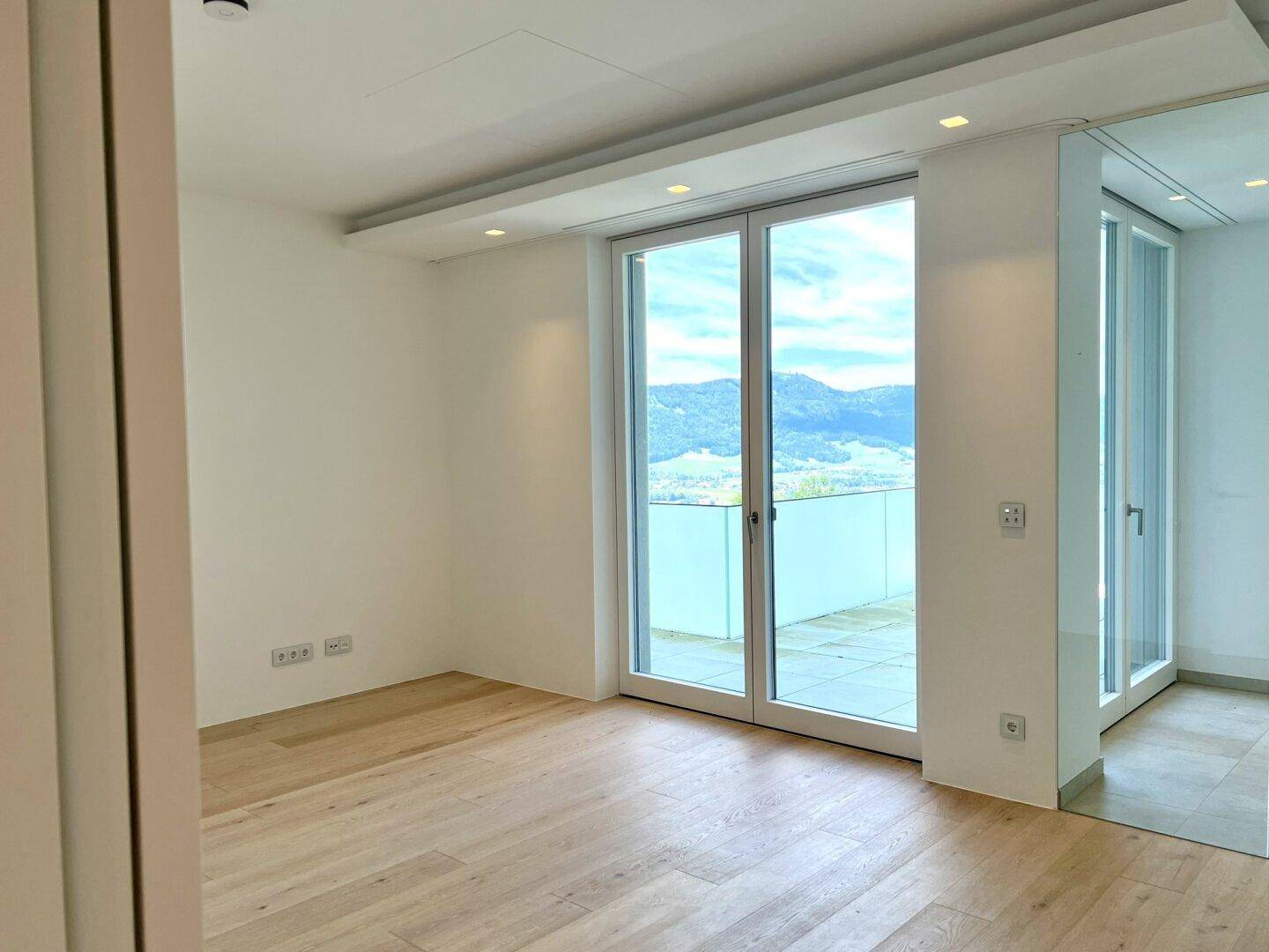 Helles Zimmer mit Holzboden und Zugang zu einem Balkon mit weitem Blick auf die Berge.