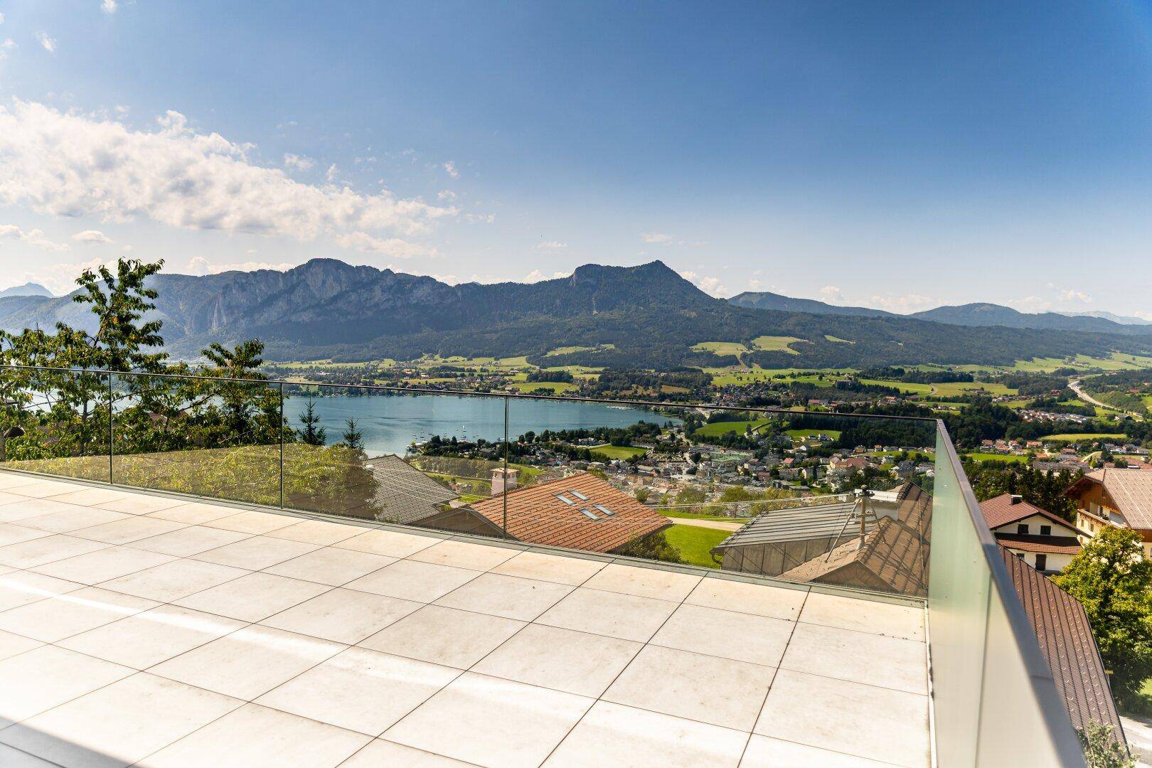 Große, geflieste Terrasse mit Glasgeländer und weitem Blick auf den See und die Berglandschaft.