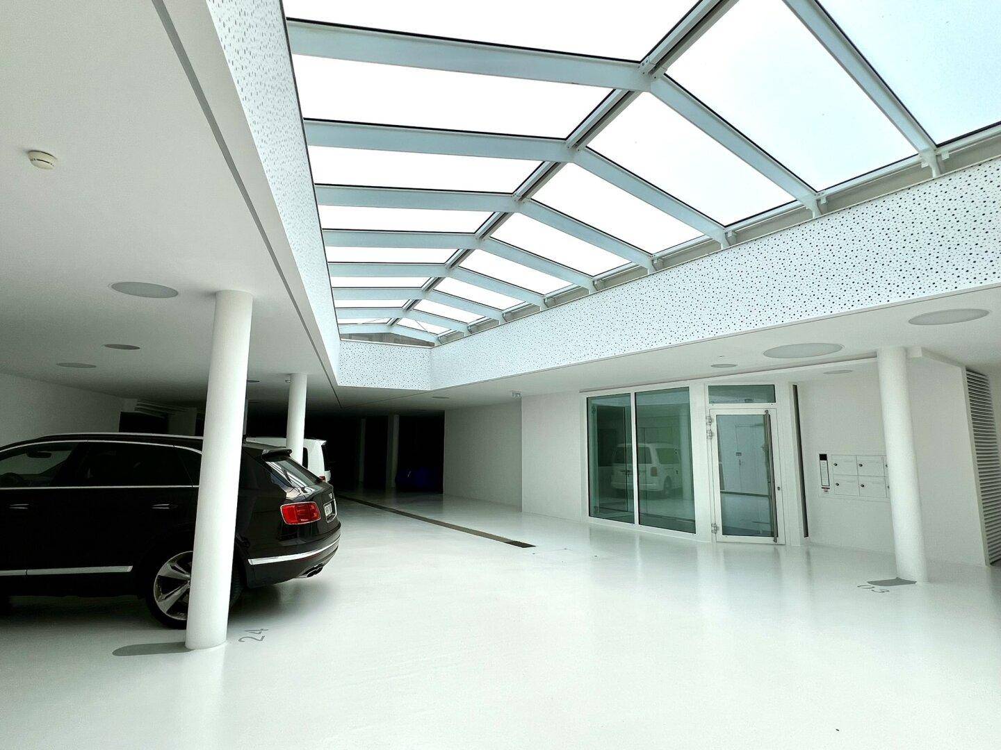 Helle Tiefgarage mit Oberlichtern, modernen Oberflächen und einem geparkten Luxusfahrzeug.