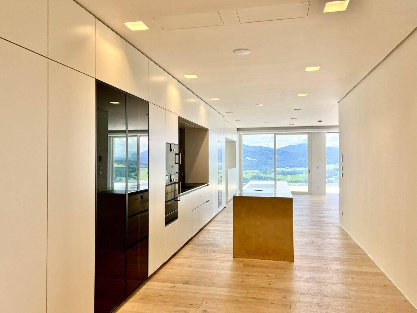 Lange, moderne Küche mit weißen Schränken, integrierten Geräten und Holzboden mit Aussicht.