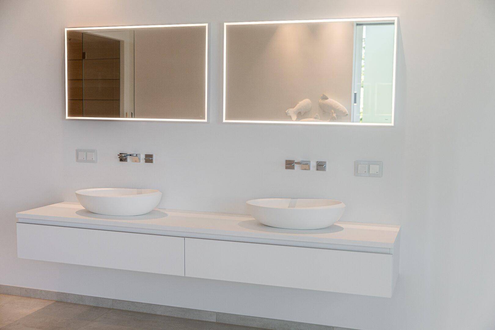 Modernes Badezimmer mit Doppelwaschbecken, beleuchteten Spiegeln und schwebendem Waschtisch in Weiß.