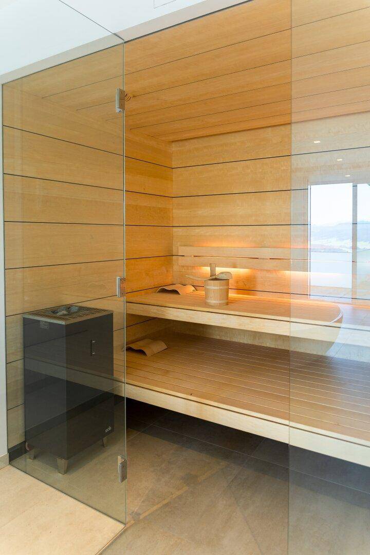 Moderne Holzsauna mit Glasfront und integrierter Beleuchtung, Teil eines luxuriösen Wellnessbereichs.