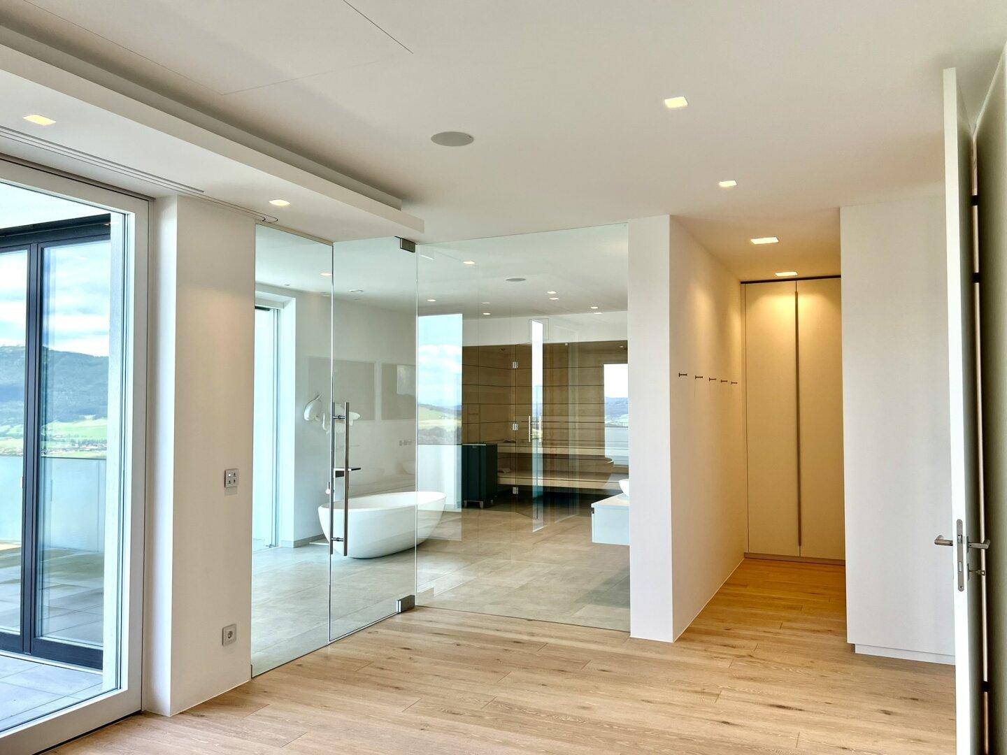Geräumiges Zimmer mit Holzboden und einer eleganten Glaswand zum luxuriösen Badezimmerbereich.