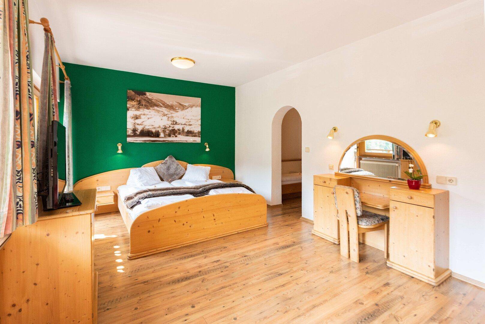 Geräumiges Schlafzimmer mit hellem Holzdoppelbett, grüner Akzentwand und Holzboden.