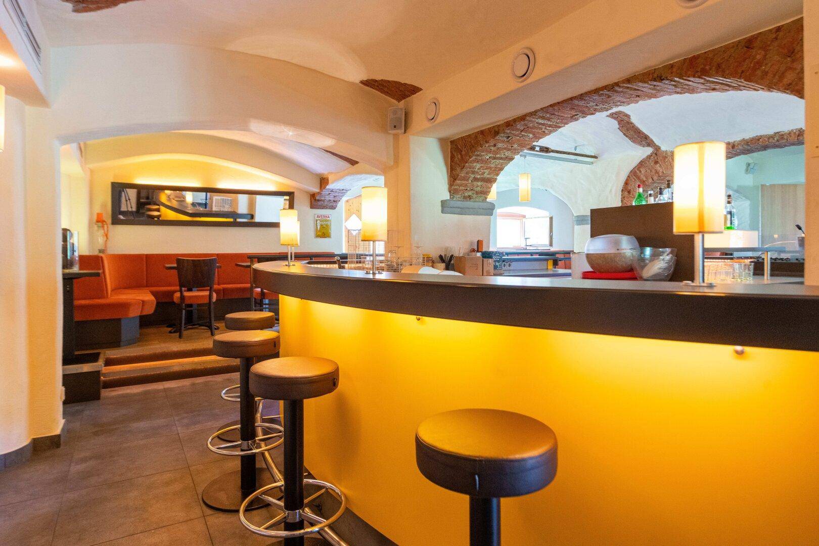 Rustikale Bar mit beleuchteter Theke, hohen Barhockern und gewölbten Ziegeldecken.