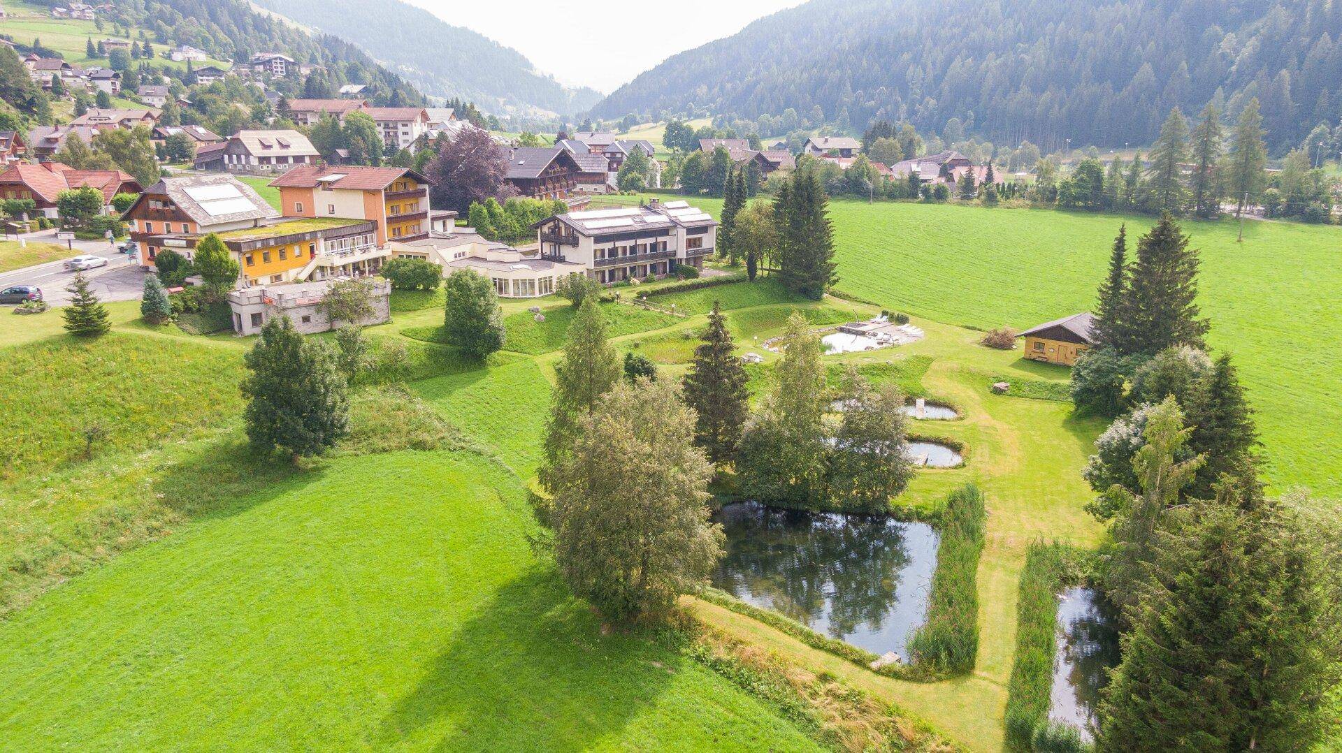 Luftaufnahme der weitläufigen Hotelanlage mit Teichen, Wiesen und umliegender Berglandschaft.