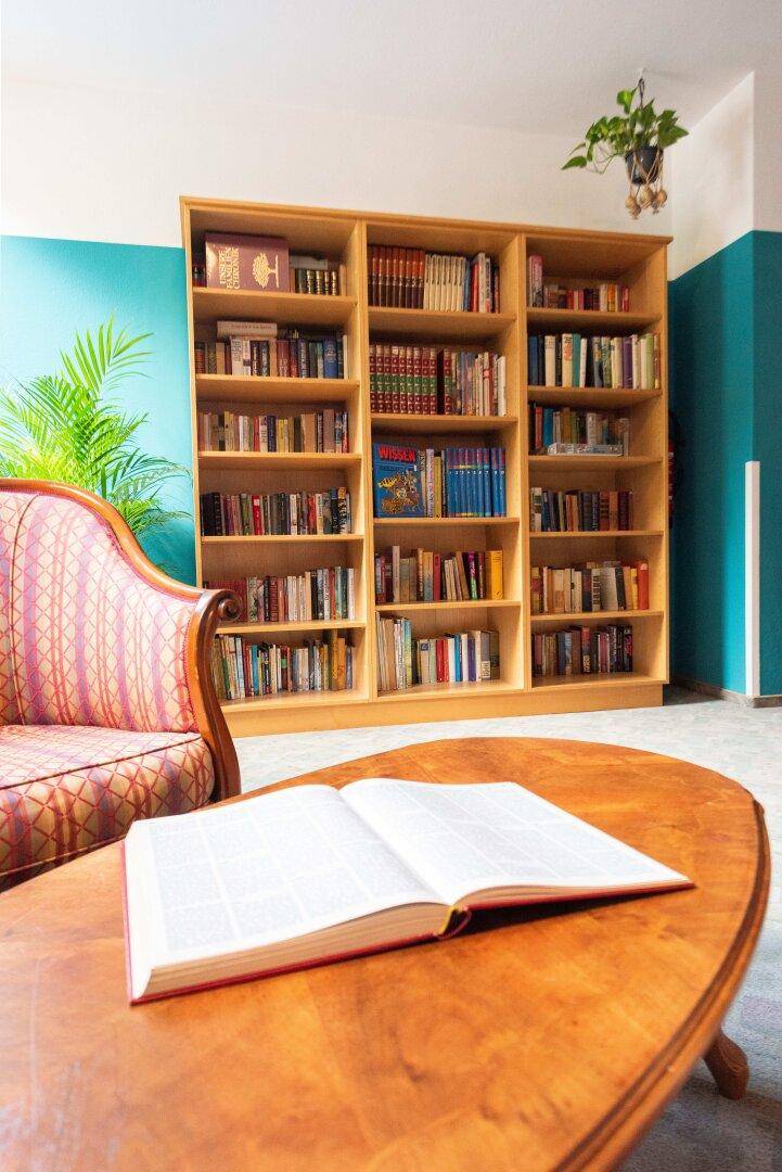 Heller Raum mit großem Bücherregal, bequemen Sessel und Holztisch, ideal zum Lesen.