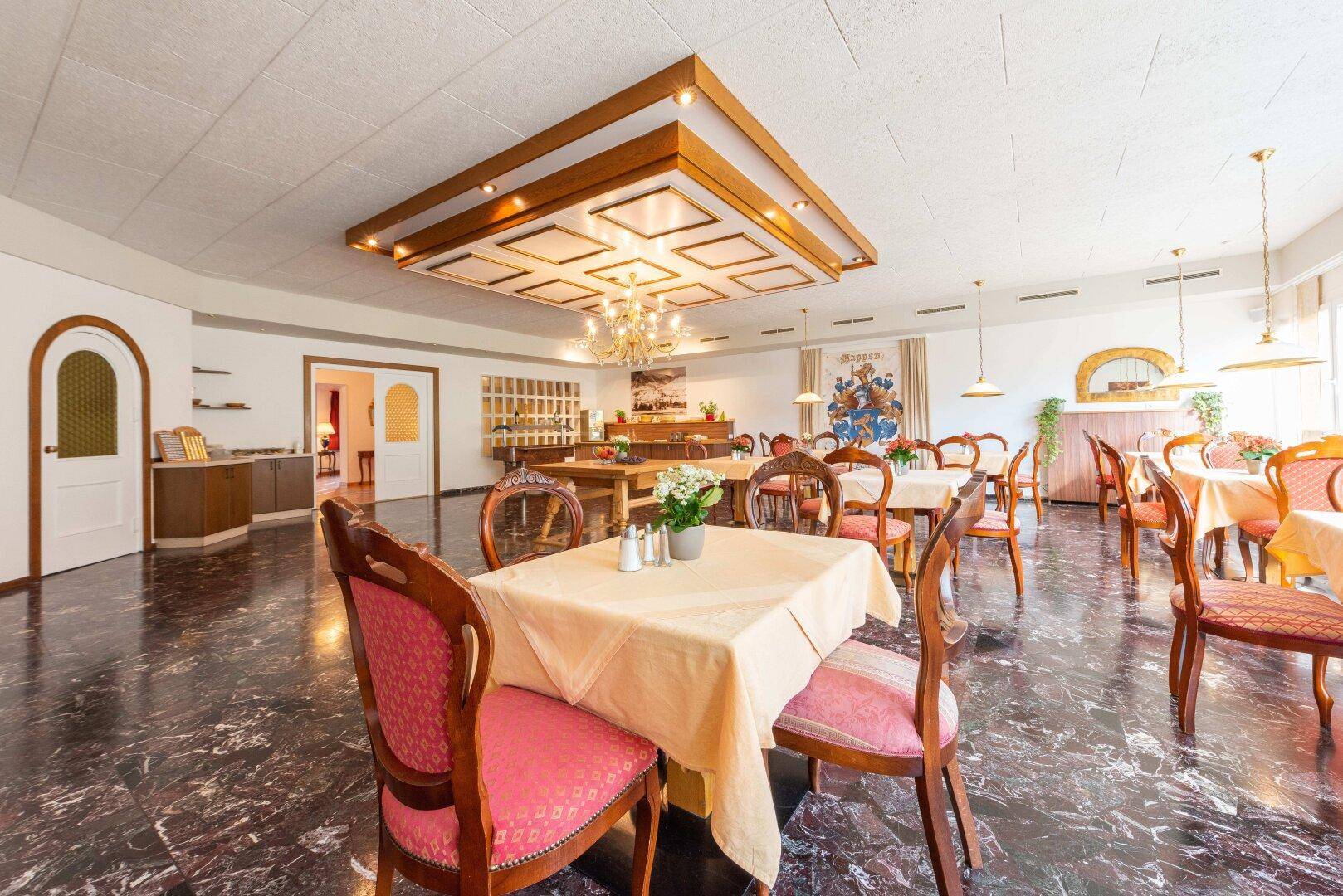 Großer Speisesaal mit eleganten Holztischen, gepolsterten Stühlen und dunklem Marmorboden.