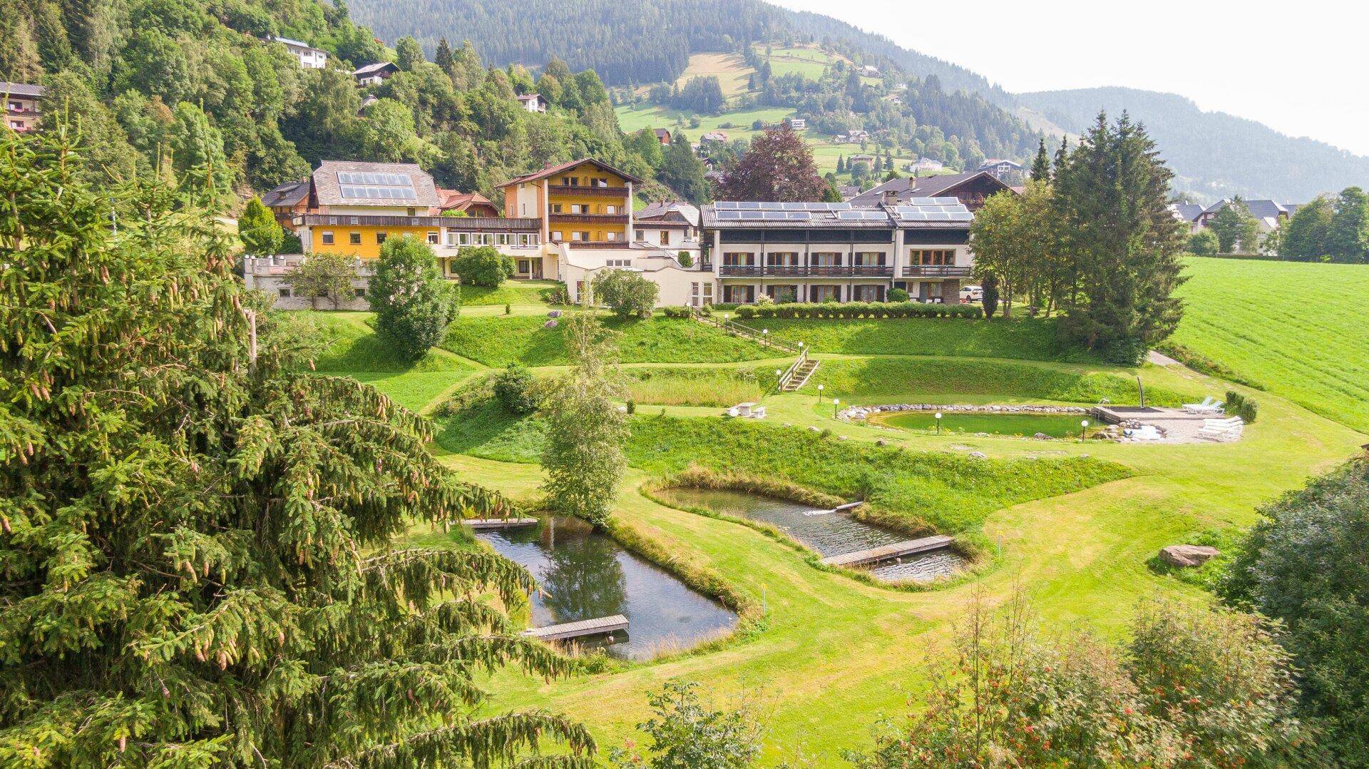 Weitläufige Hotelanlage eingebettet in eine grüne Berglandschaft mit Teichen und Solaranlagen auf den Dächern.
