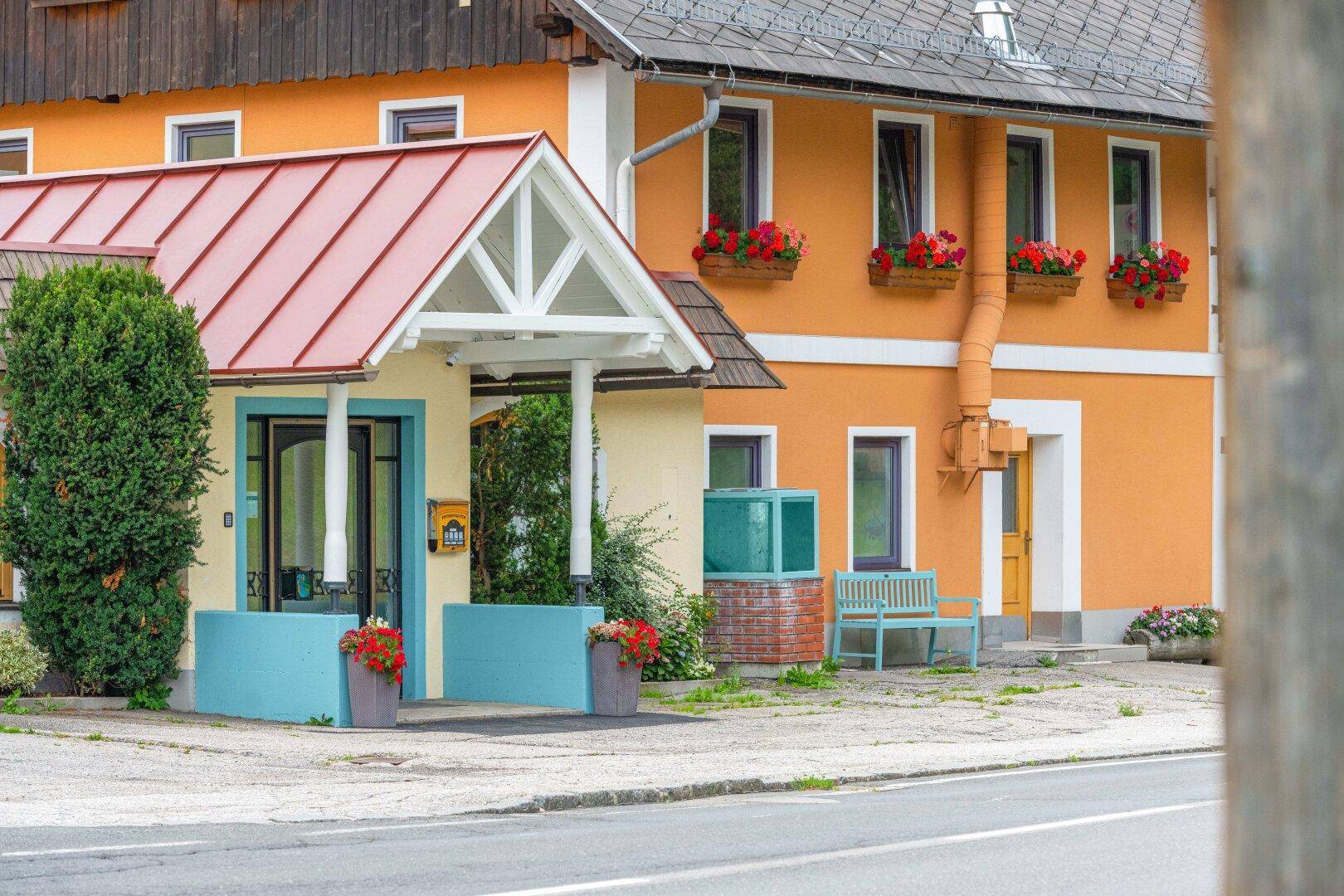 Farbenfrohe Fassade eines Gebäudes mit einem kleinen Vordach und Blumenkästen an den Fenstern.