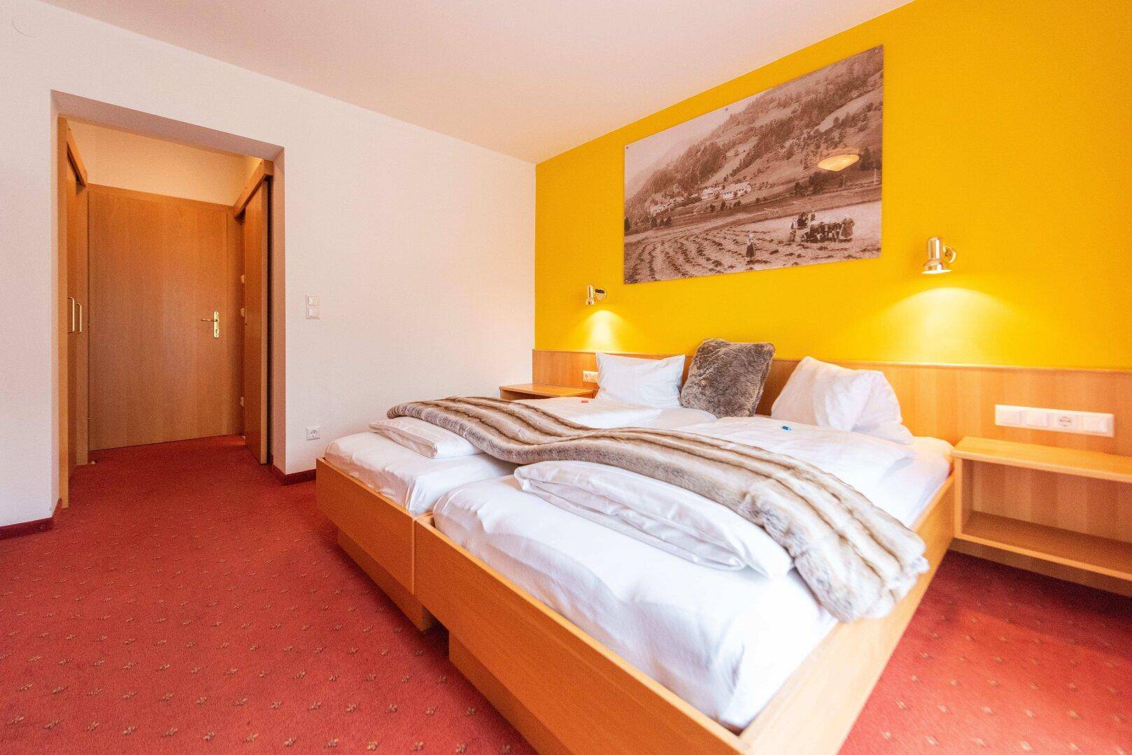 Gemütliches Schlafzimmer mit zwei Einzelbetten, gelber Akzentwand und rotem Teppichboden.