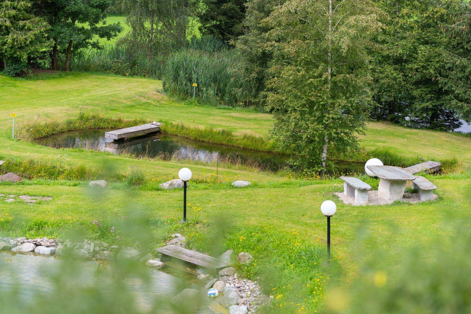 Weitläufige Gartenanlage mit mehreren Teichen, Rasenflächen und einem Steintisch mit Bänken.