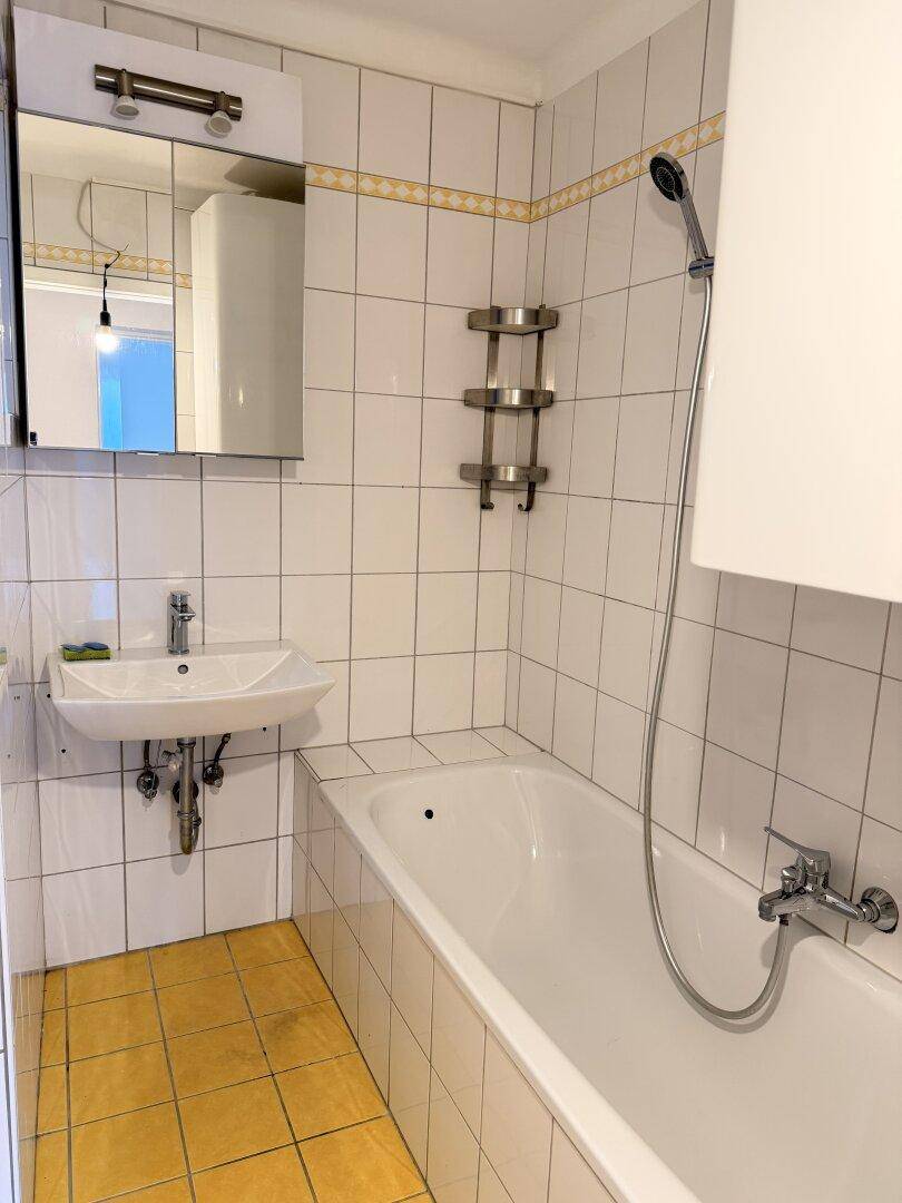 Gefliestes Badezimmer mit Badewanne, Duschvorrichtung, Waschbecken und Spiegelschrank.