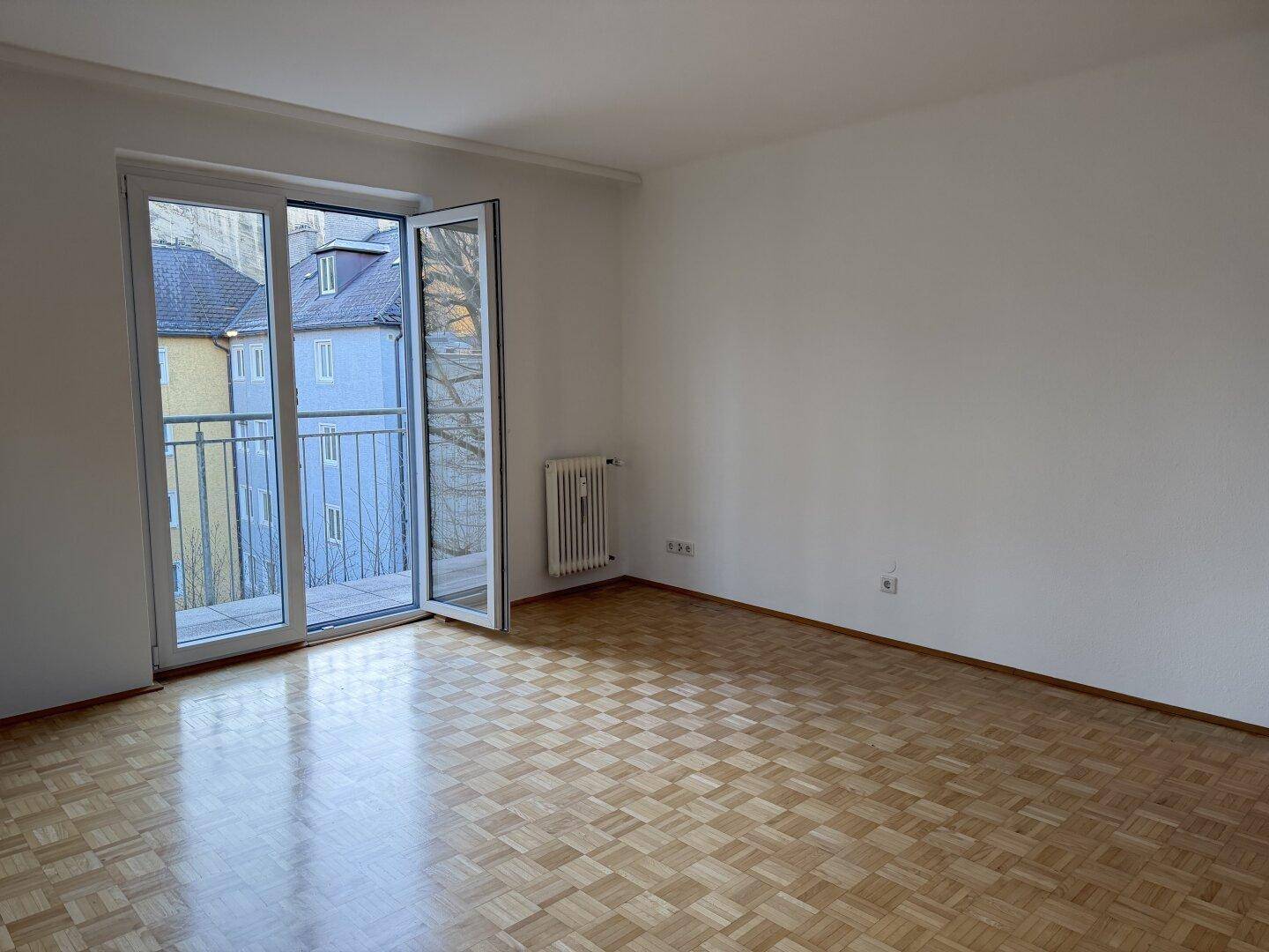 Helles Wohnzimmer mit Parkettboden und Zugang zu einem französischen Balkon mit Metallgeländer.
