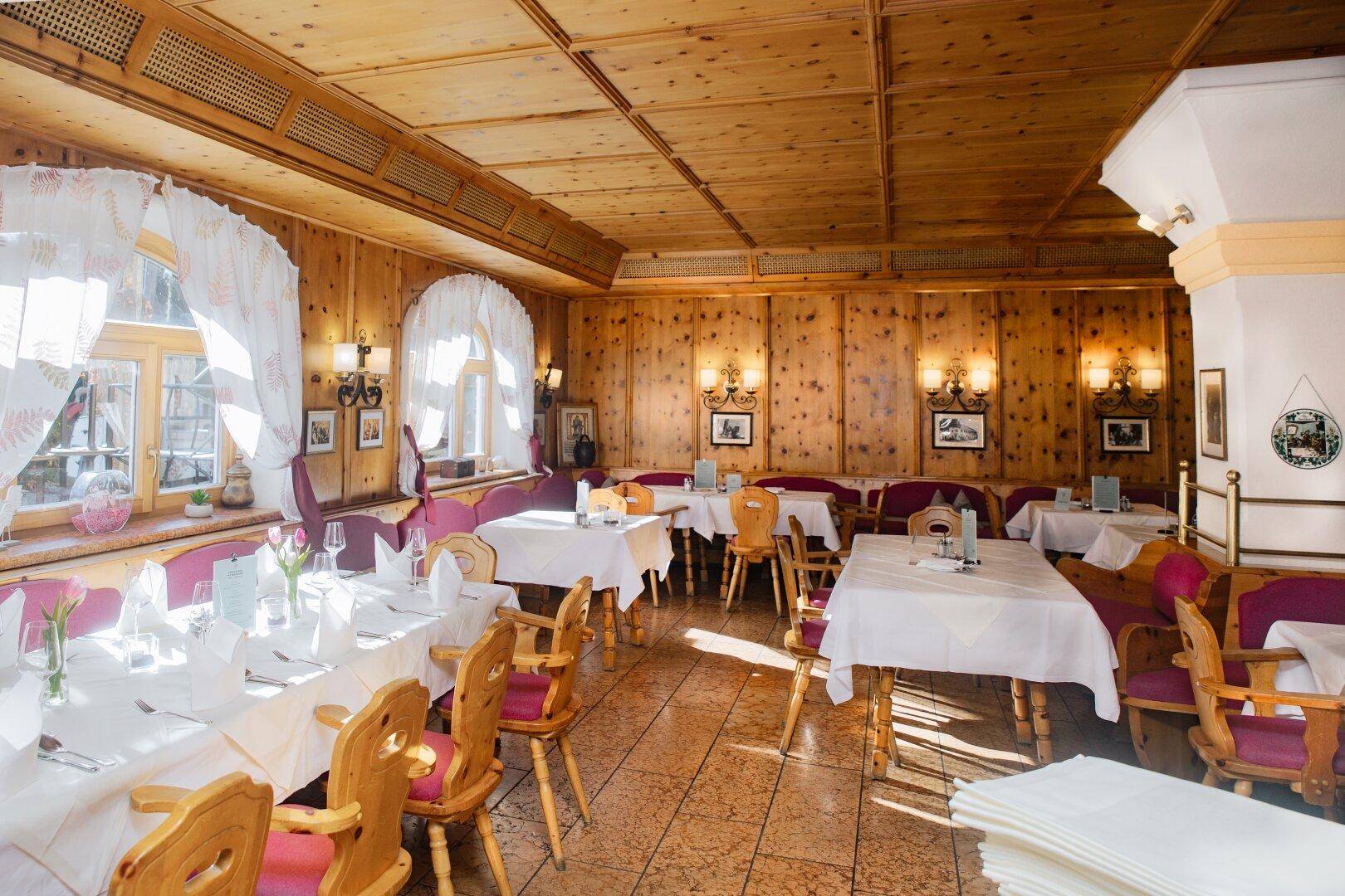 Heller Speisesaal mit holzgetäfelten Wänden und Decke, sowie Tischen mit rosa gepolsterten Stühlen.