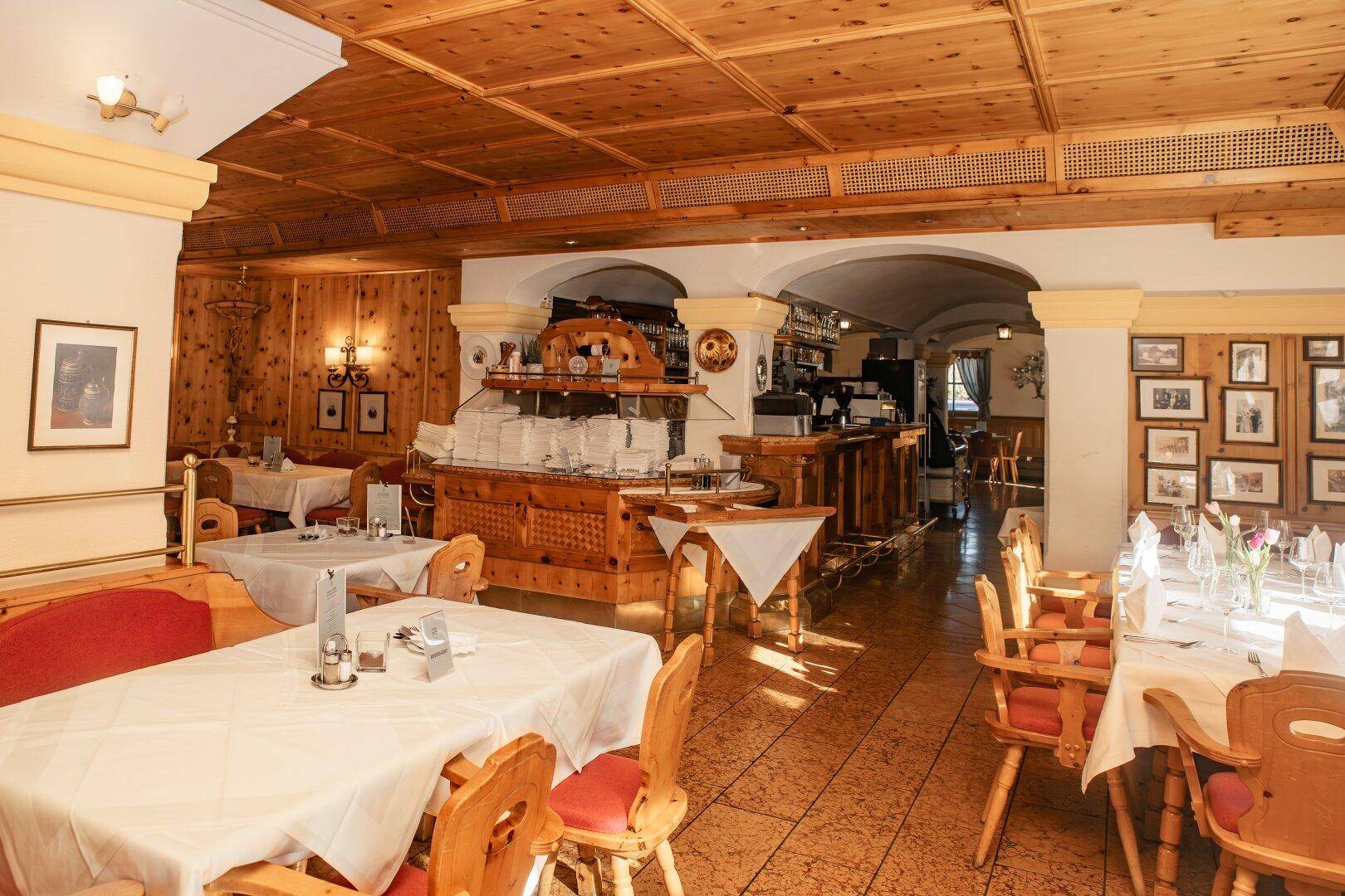 Geräumiger Speisesaal mit Holztäfelung, vielen Tischen und einem Barbereich im Hintergrund.