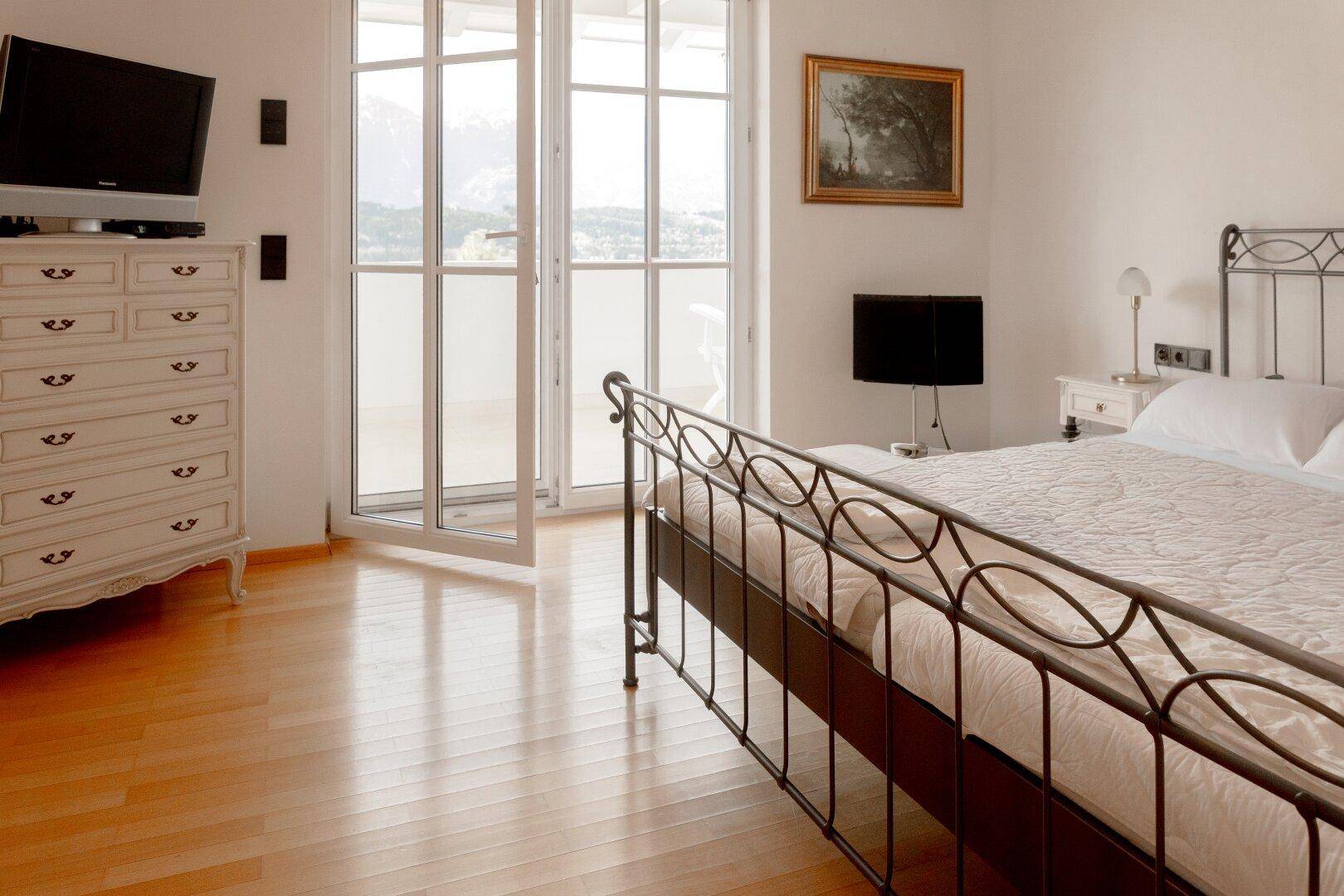 Gemütliches Schlafzimmer mit schmiedeeisernem Bett, Holzboden und Zugang zum Balkon.