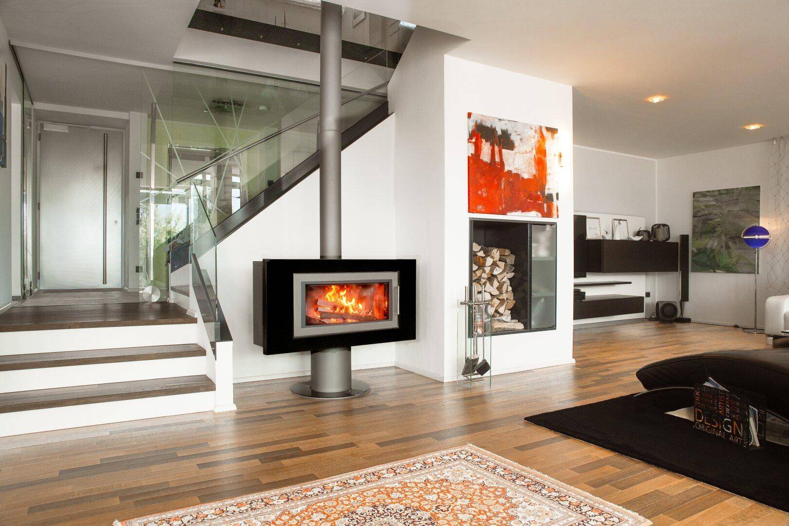 Moderner Wohnbereich mit freistehendem Kamin, Holzfußboden und Treppe mit Glasgeländer.