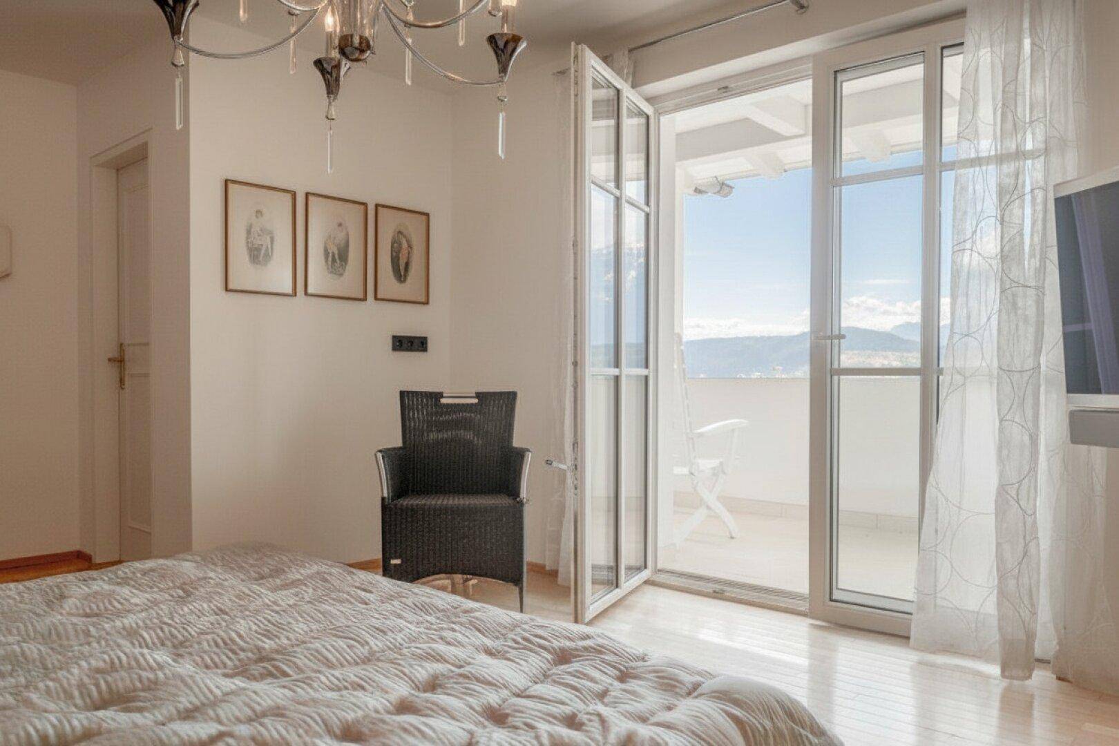 Helles Schlafzimmer mit Doppelbett, Balkonzugang und Blick auf die umliegende Landschaft.