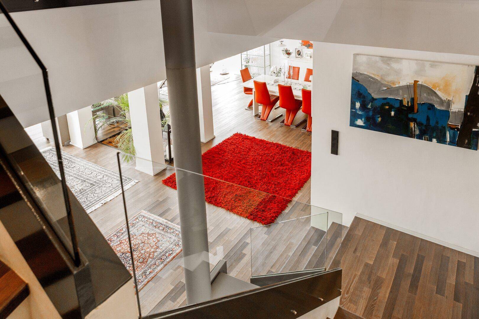 Blick von der Treppe in den offenen Wohn- und Essbereich mit Holzboden und rotem Teppich.