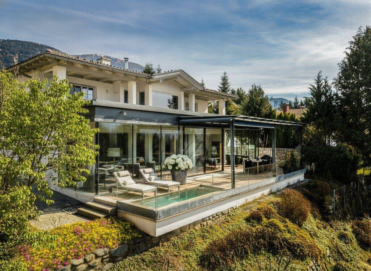 Elegantes Haus mit moderner Glasfassade, Holzterrasse und kleinem Pool in alpiner Umgebung.