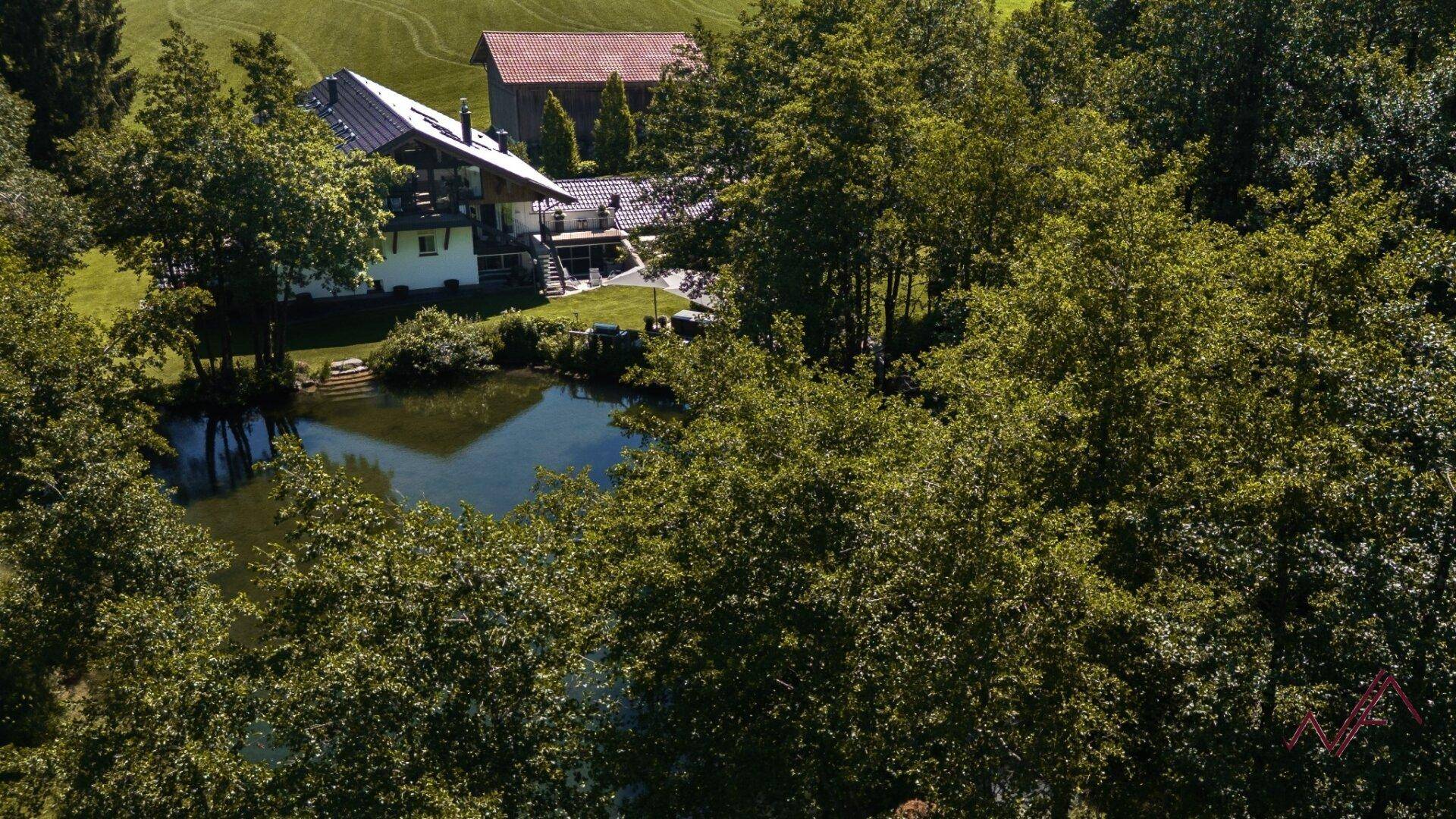Idyllische Luftaufnahme des Anwesens mit einem natürlichen Teich, umgeben von üppigem Grün und Bäumen.