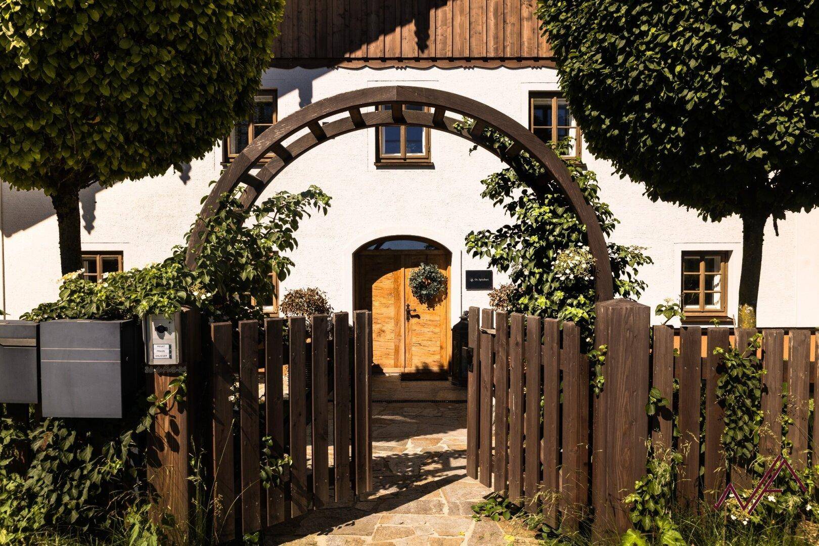 Charmantes Holztor mit Bogen und gepflastertem Weg führt zum Hauseingang mit Holztür.