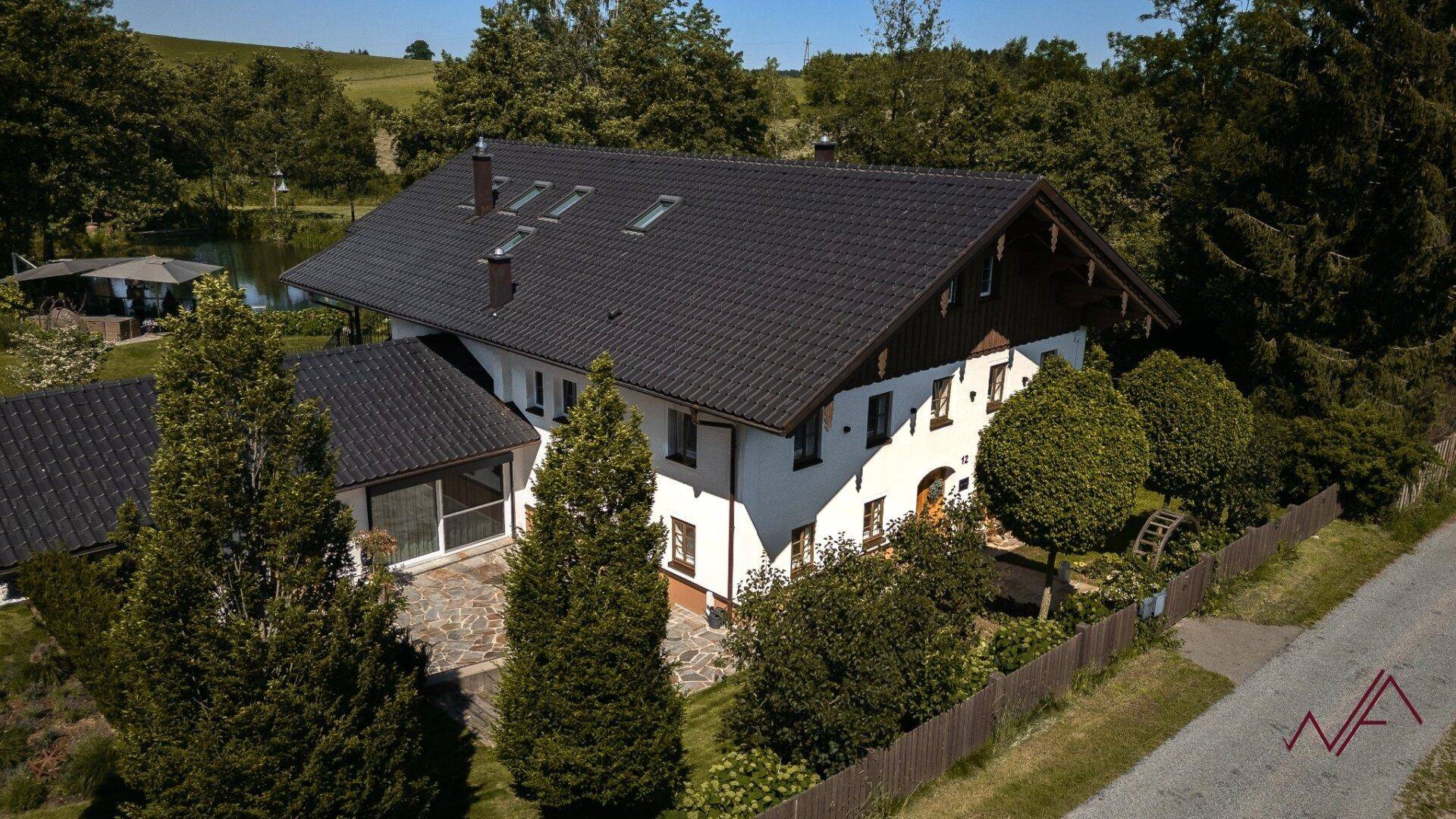 Das Anwesen von oben, umgeben von Bäumen und einem Teich, mit traditioneller Architektur und gepflegtem Garten.